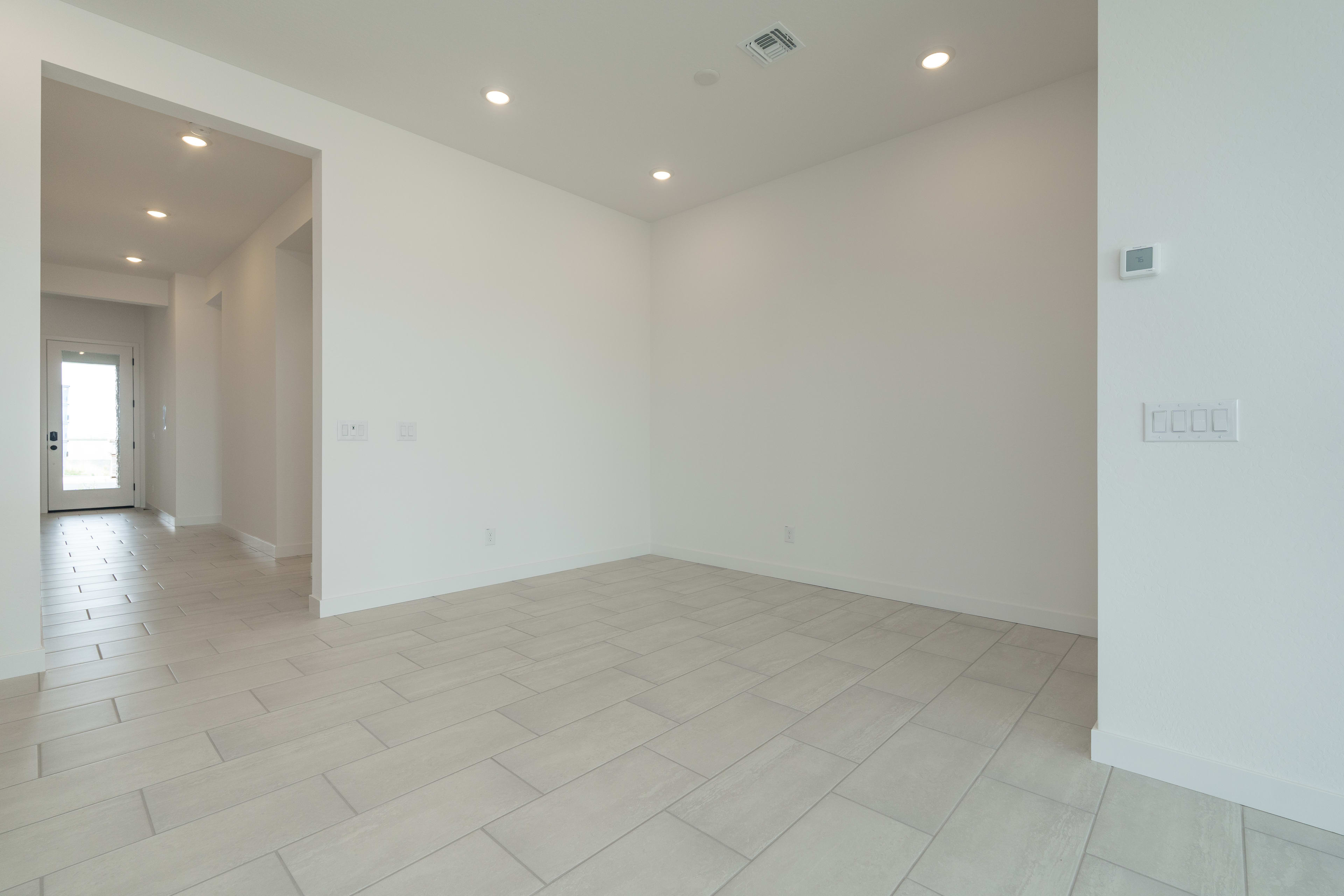 Light-colored tile flooring fills the foreground of an empty, modern room with a hallway visible in the background.