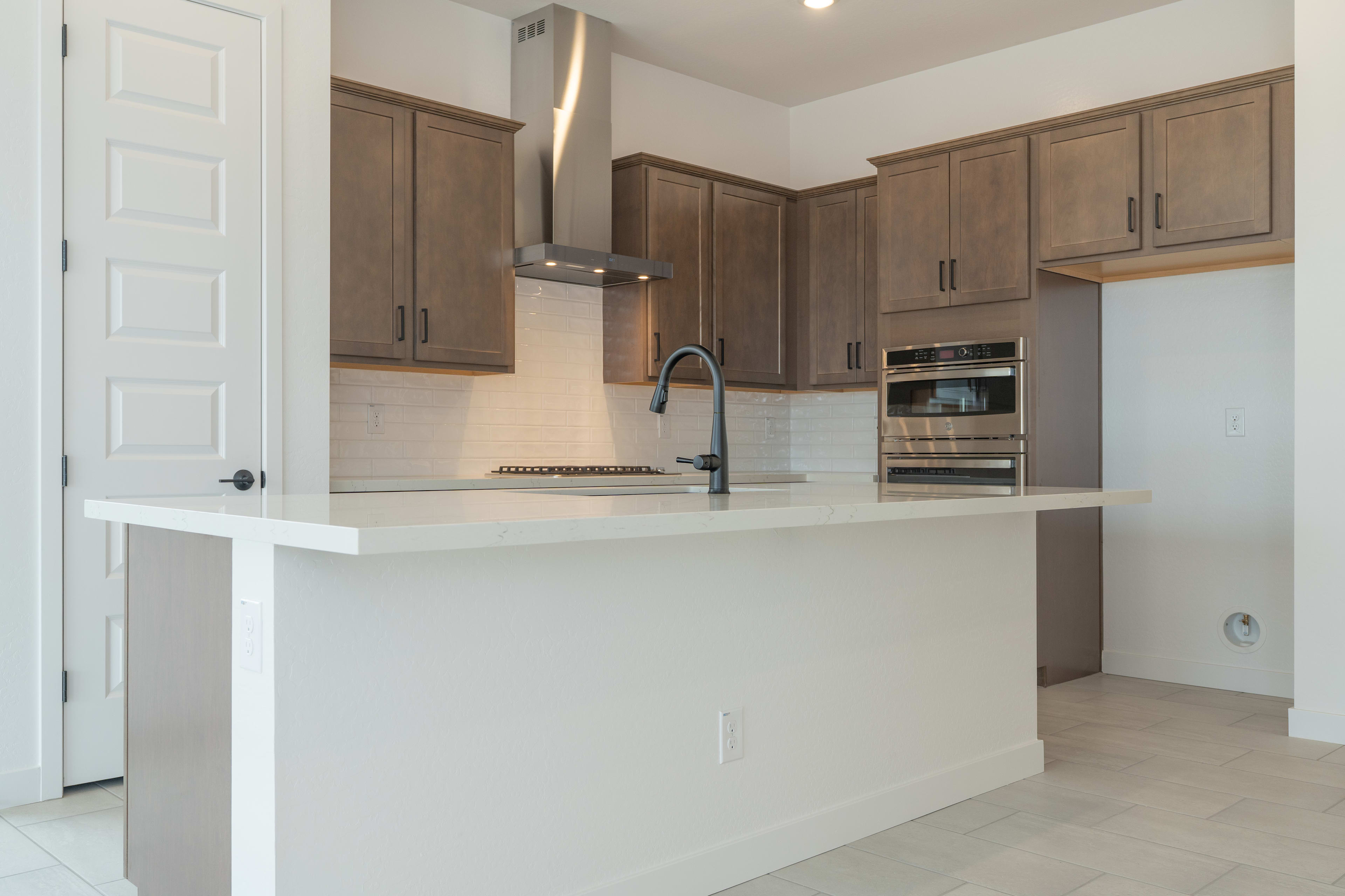 A modern kitchen features a white island in the foreground and gray cabinetry with stainless steel appliances in the background.