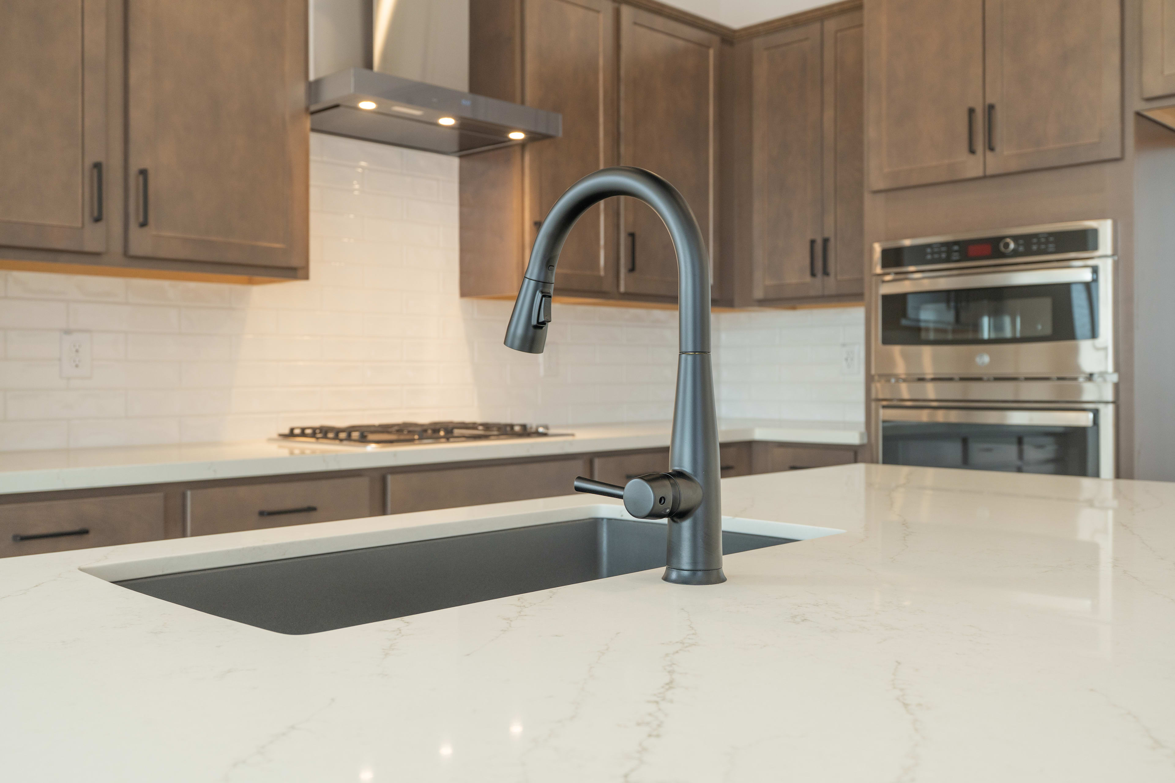 A modern kitchen sink with a dark faucet is in the foreground, while stainless steel appliances and wooden cabinets fill the background.