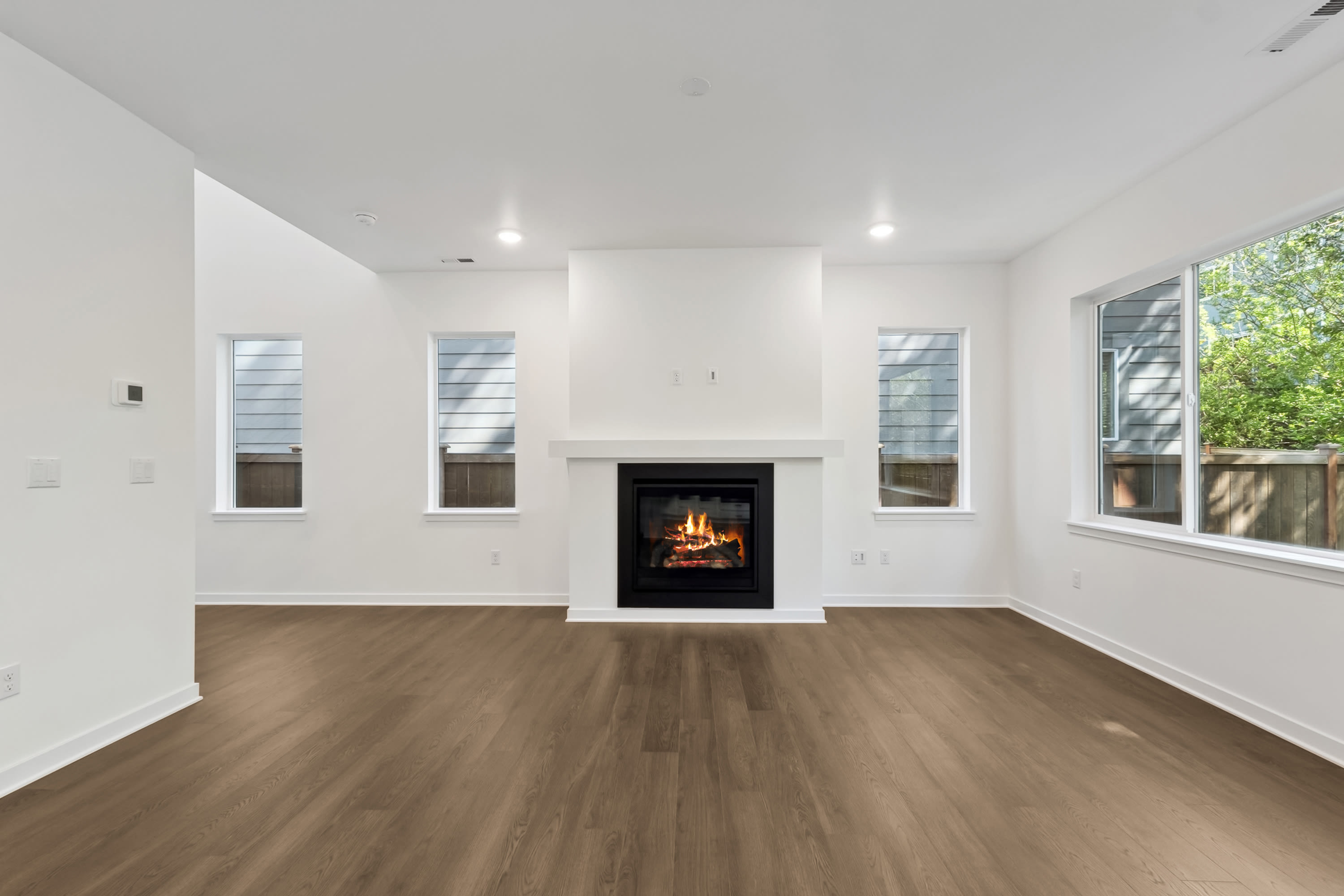 A modern living room with a lit fireplace and large windows overlooking greenery.