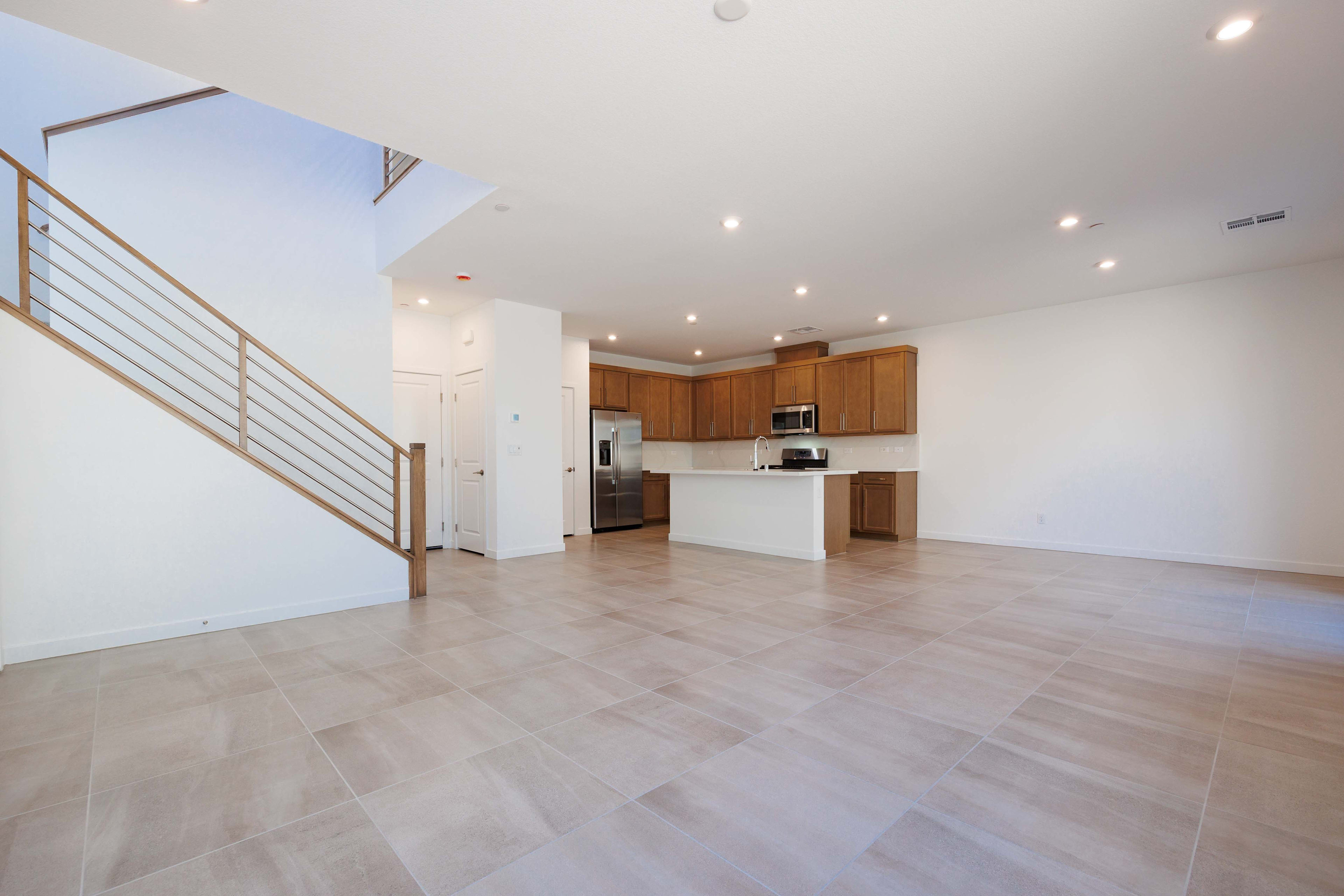 A modern, open-concept living space with a tiled floor in the foreground and a kitchen with wooden cabinets in the background.