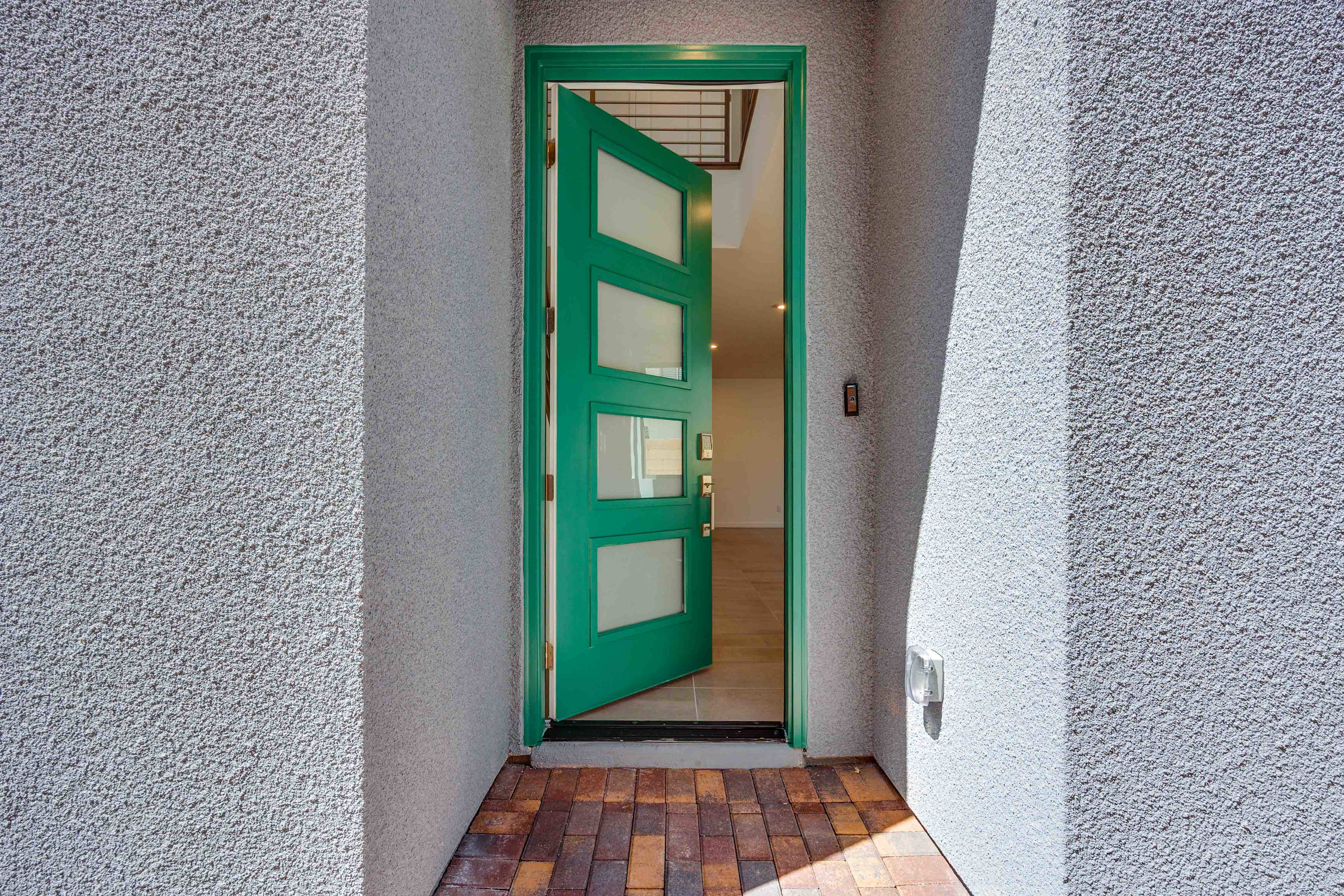 A bright green door with glass panels stands open on a textured wall, revealing a glimpse of a hallway with tiled flooring.