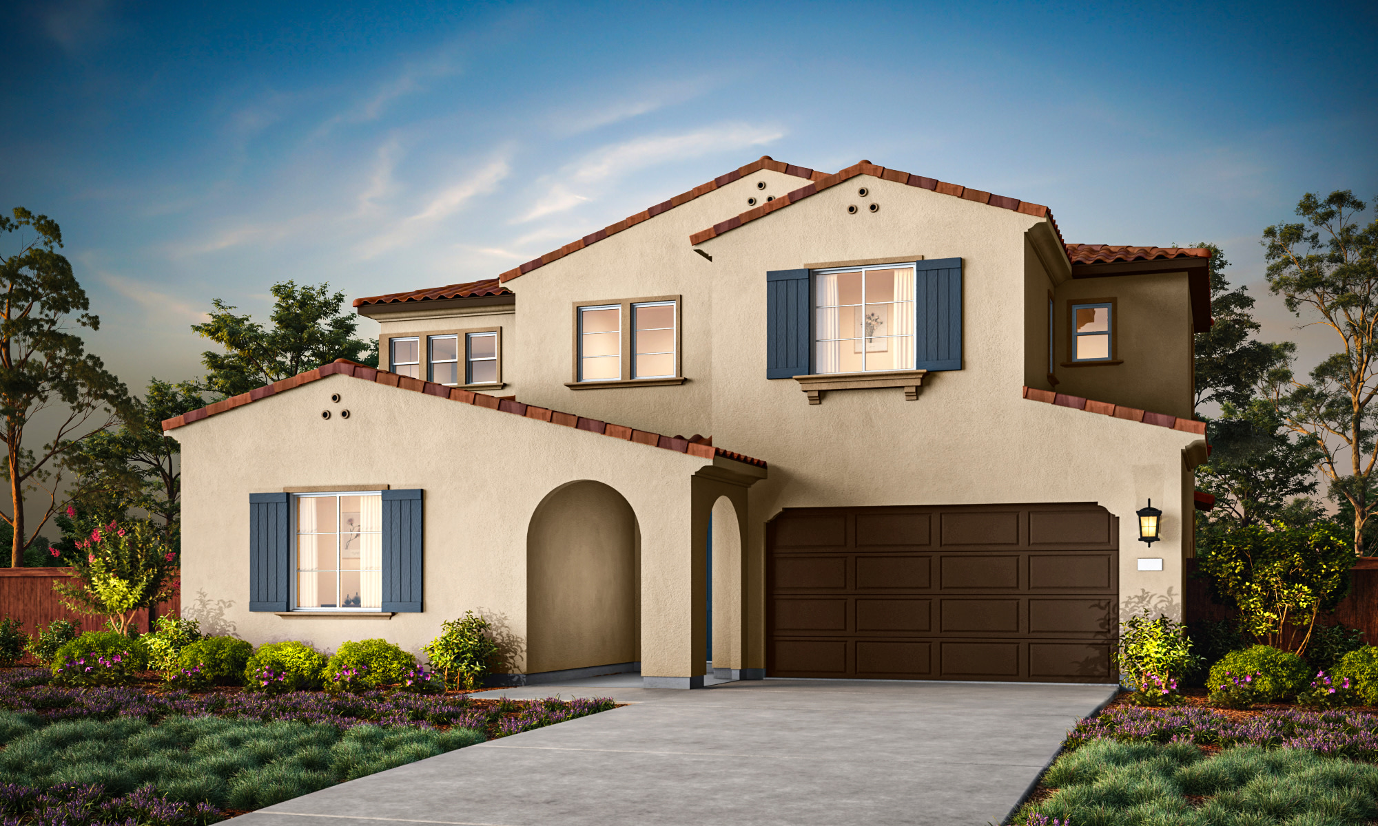 A two-story Mediterranean-style house with a red tile roof, white stucco exterior, and a garage door stands in a well-landscaped yard with shrubs and trees in the foreground.