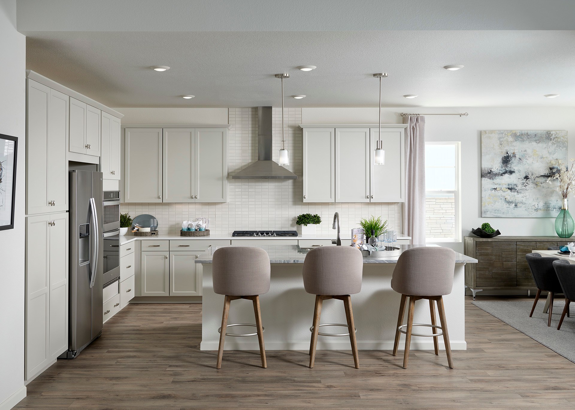 A modern, open-concept kitchen with white cabinets, a large island with bar stools, and a dining area visible in the background.