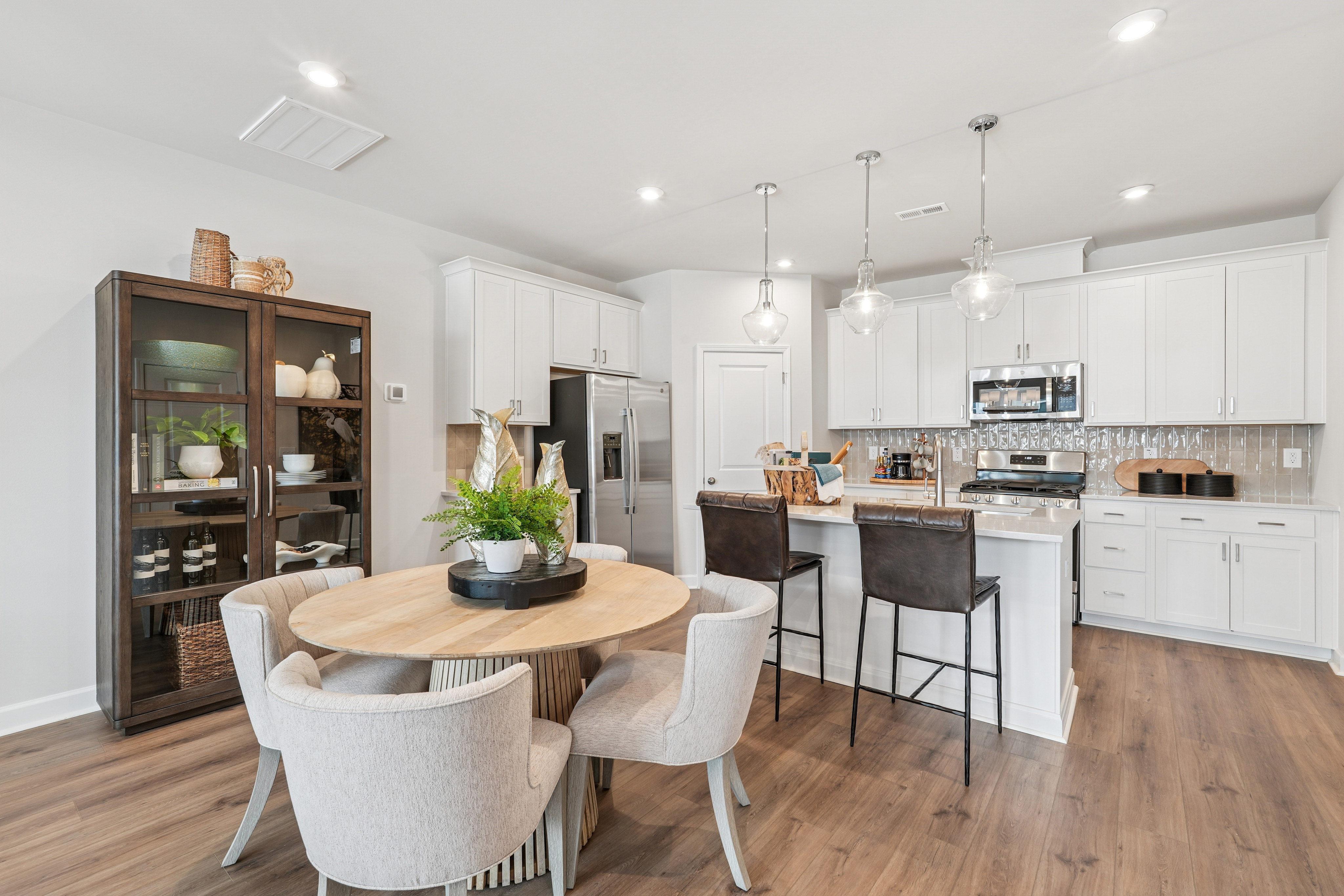 A modern, open-concept kitchen and dining area with white cabinets, a wooden dining table, and comfortable upholstered chairs.