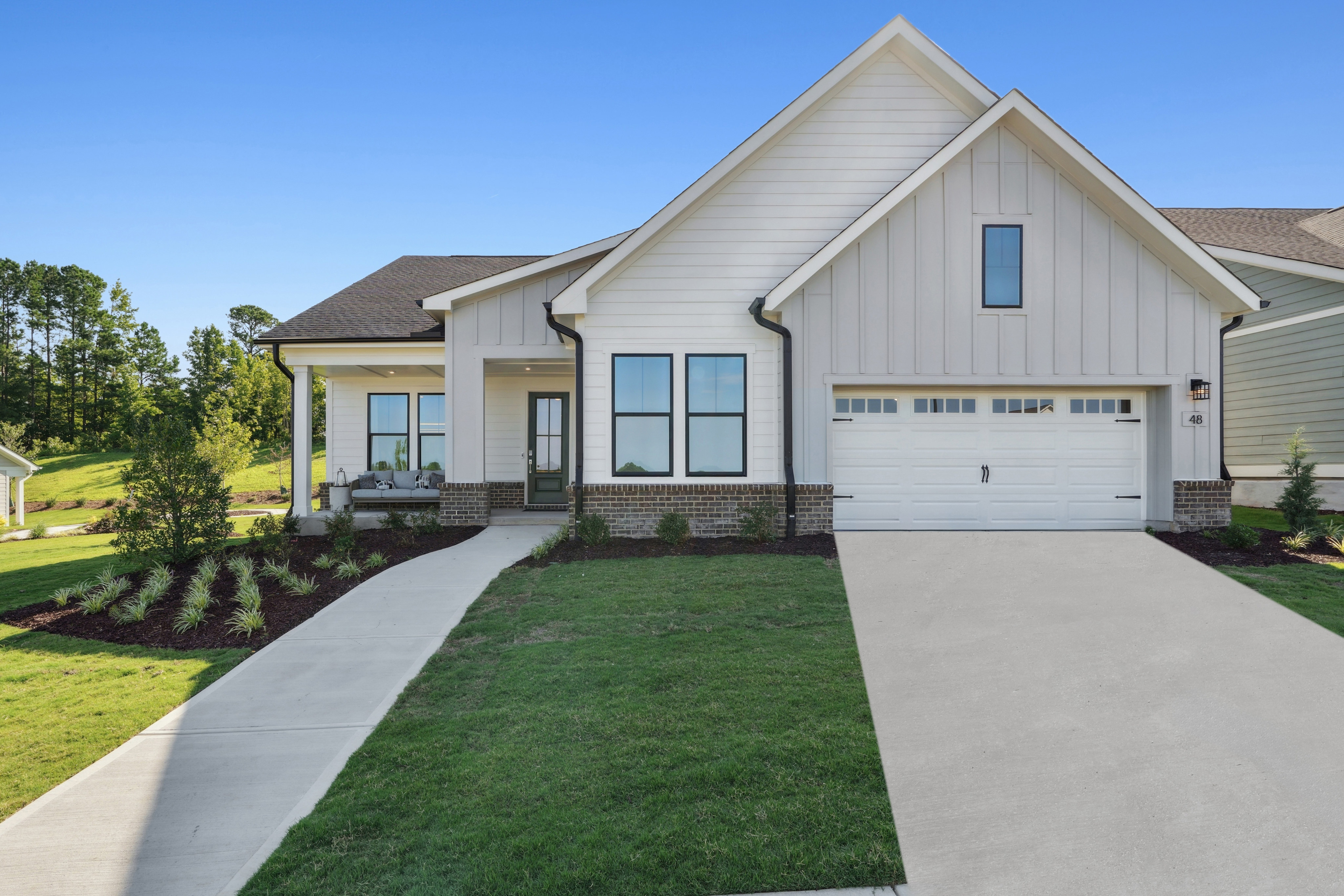 A modern, two-story house with a white exterior, a gabled roof, and a well-manicured lawn in the foreground, set against a backdrop of lush greenery and a clear blue sky.