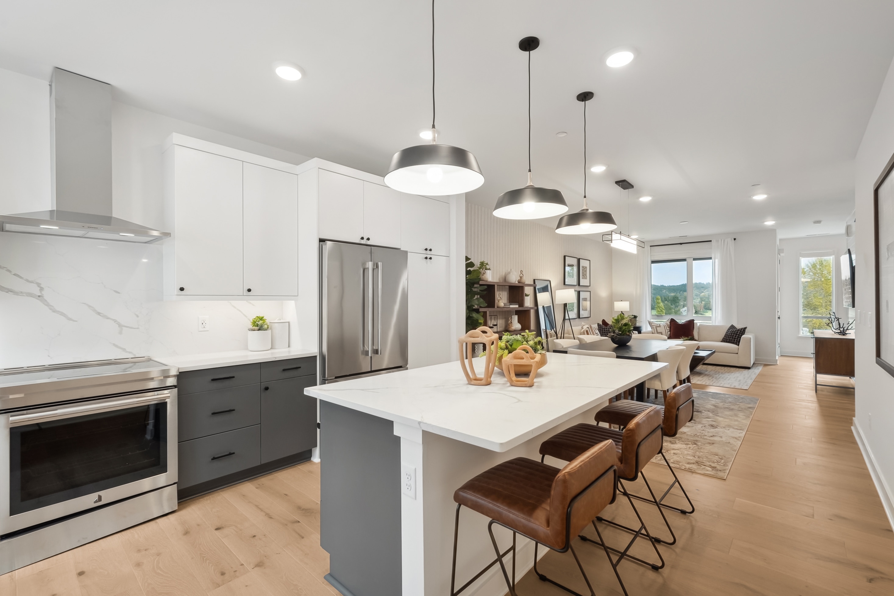 A modern, open-concept kitchen with a large island, stainless steel appliances, and pendant lighting, leading into a spacious living area with hardwood floors and a cozy seating arrangement.