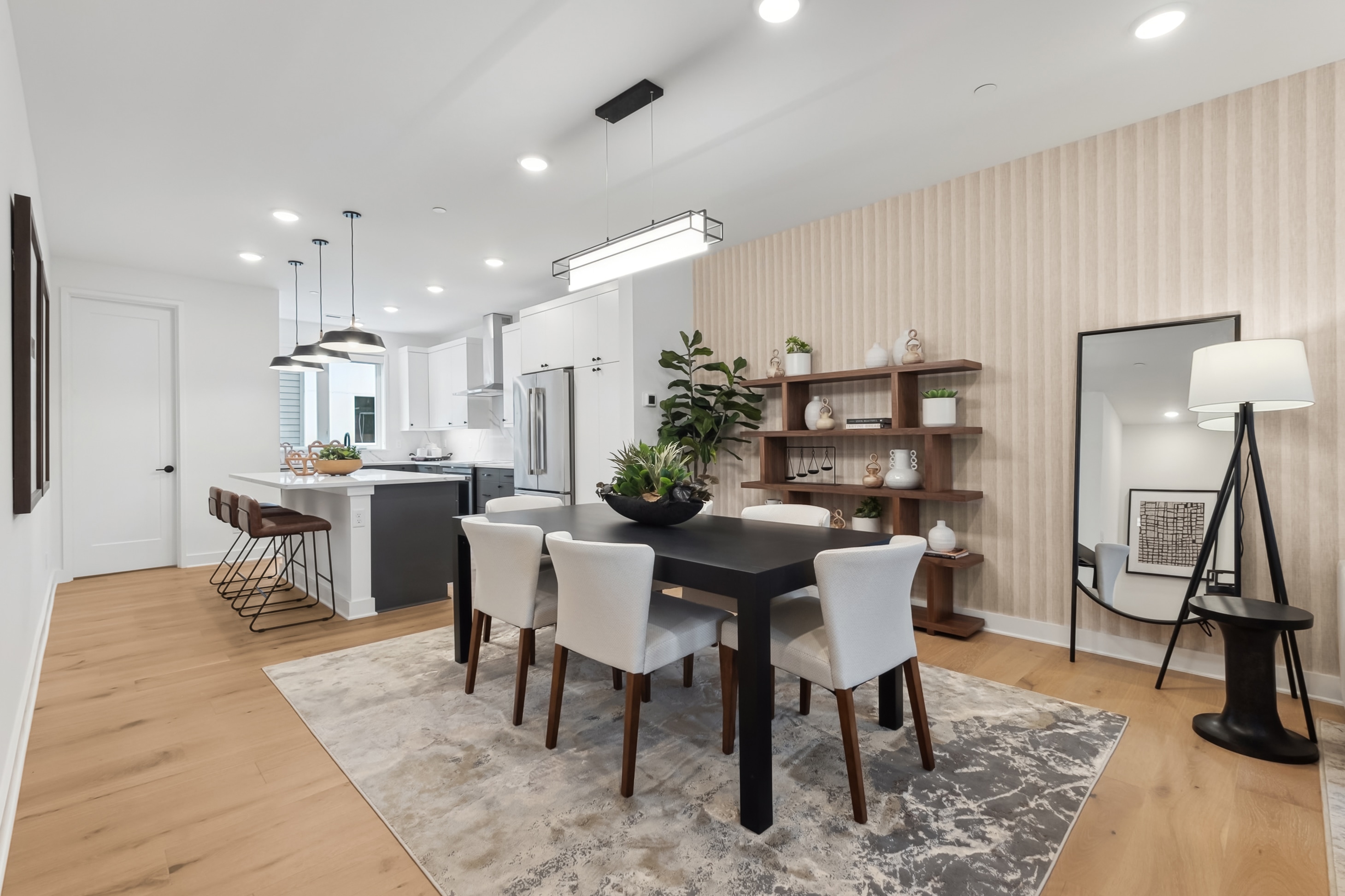 A modern and stylish dining room with a wooden table, upholstered chairs, and a sleek kitchen area with shelving and appliances in the background.
