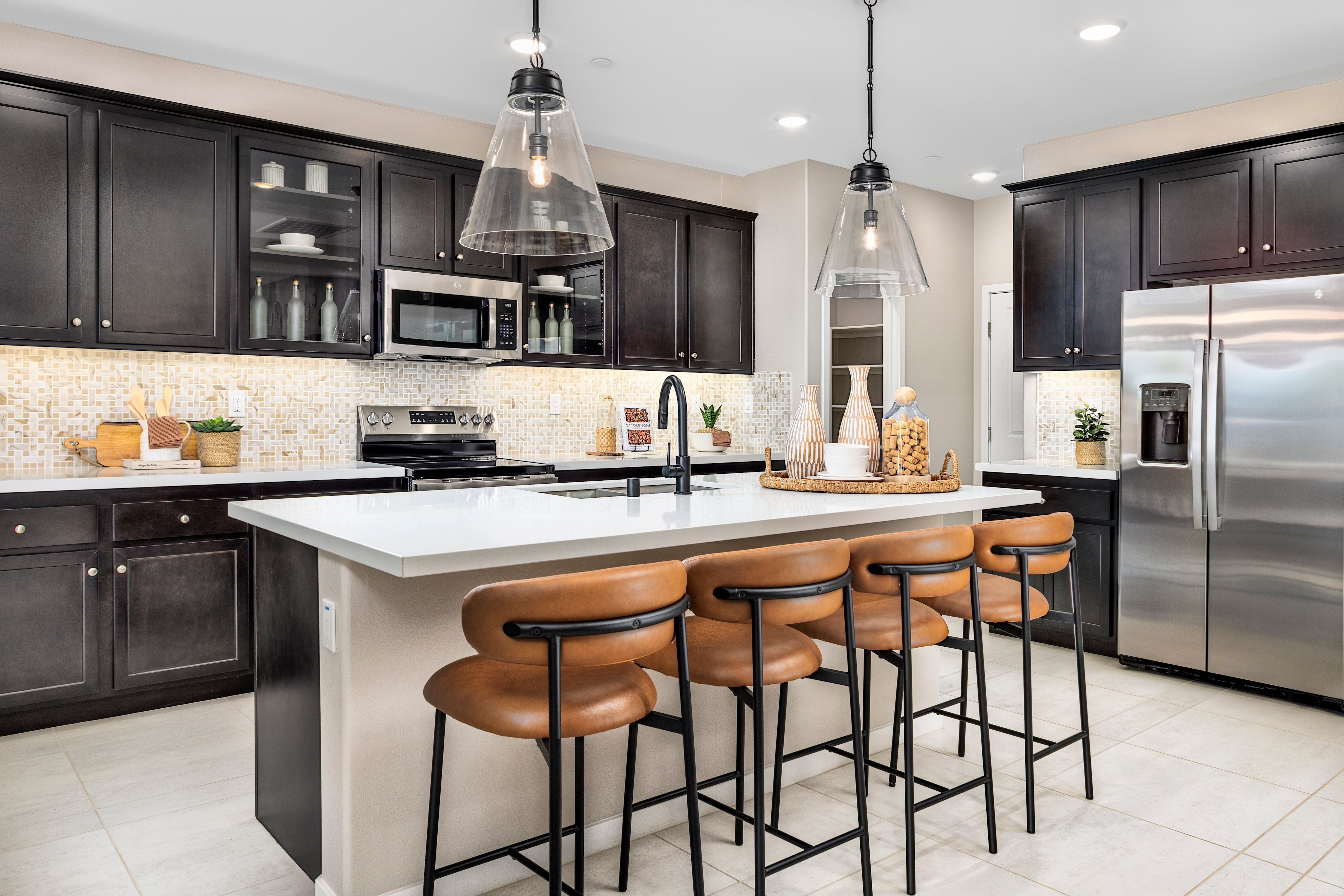 A modern and stylish kitchen with dark cabinets, a white countertop, and pendant lights illuminating the central island with bar stools.