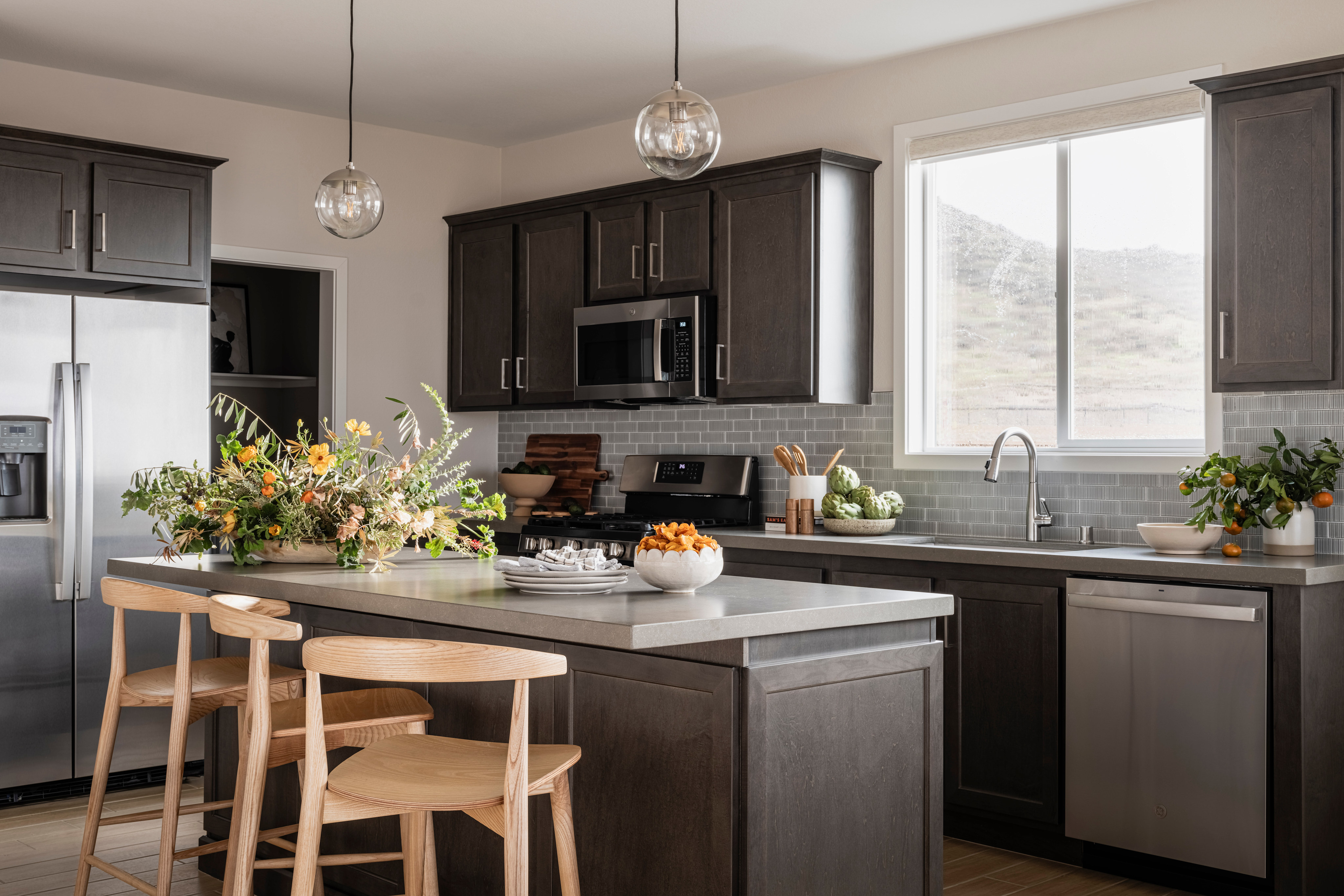 A modern and well-equipped kitchen with dark cabinets, stainless steel appliances, and a central island with stools, surrounded by a bright and airy atmosphere.