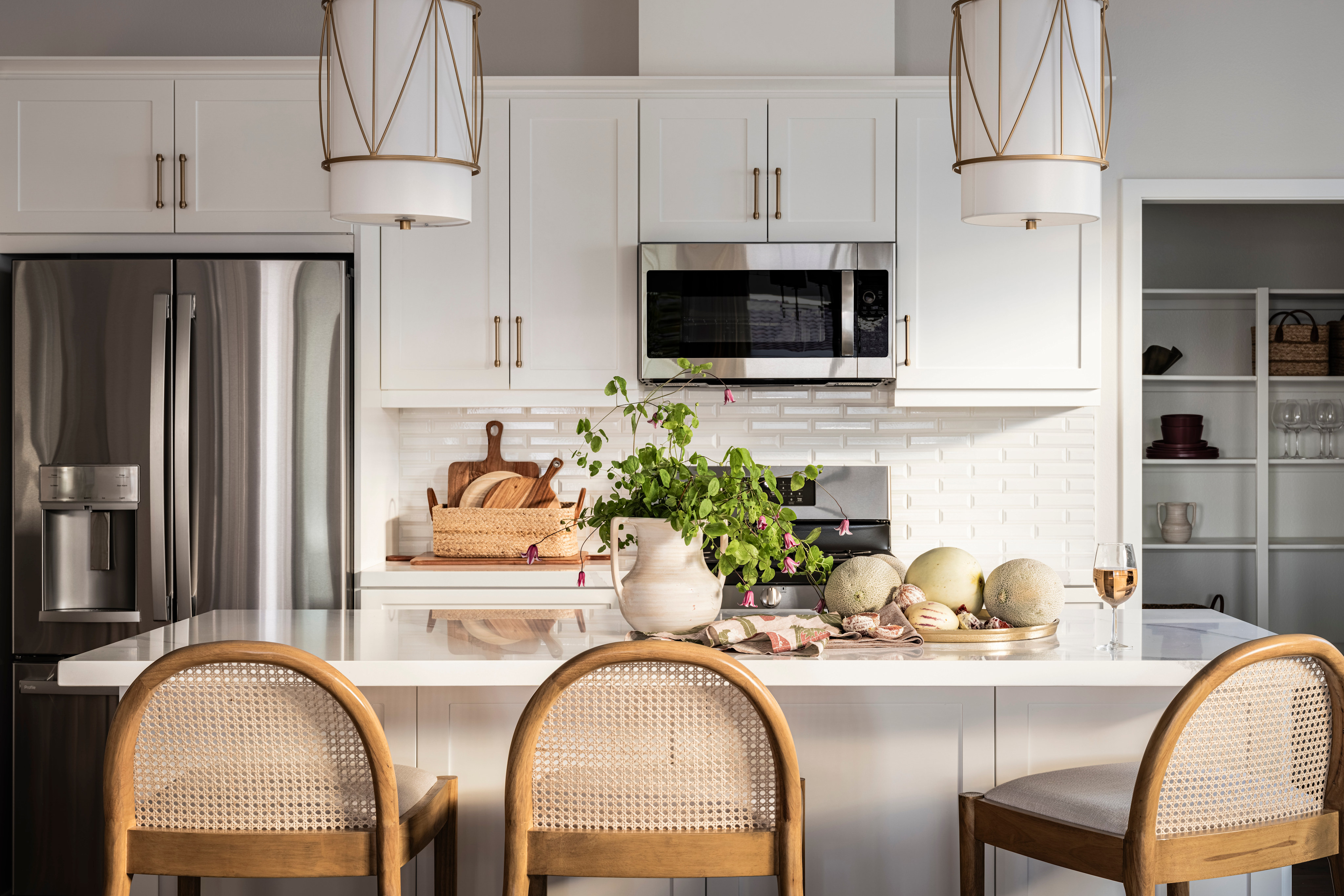 A modern, well-appointed kitchen with white cabinets, stainless steel appliances, and a central island with stools, featuring decorative elements such as plants and pottery.