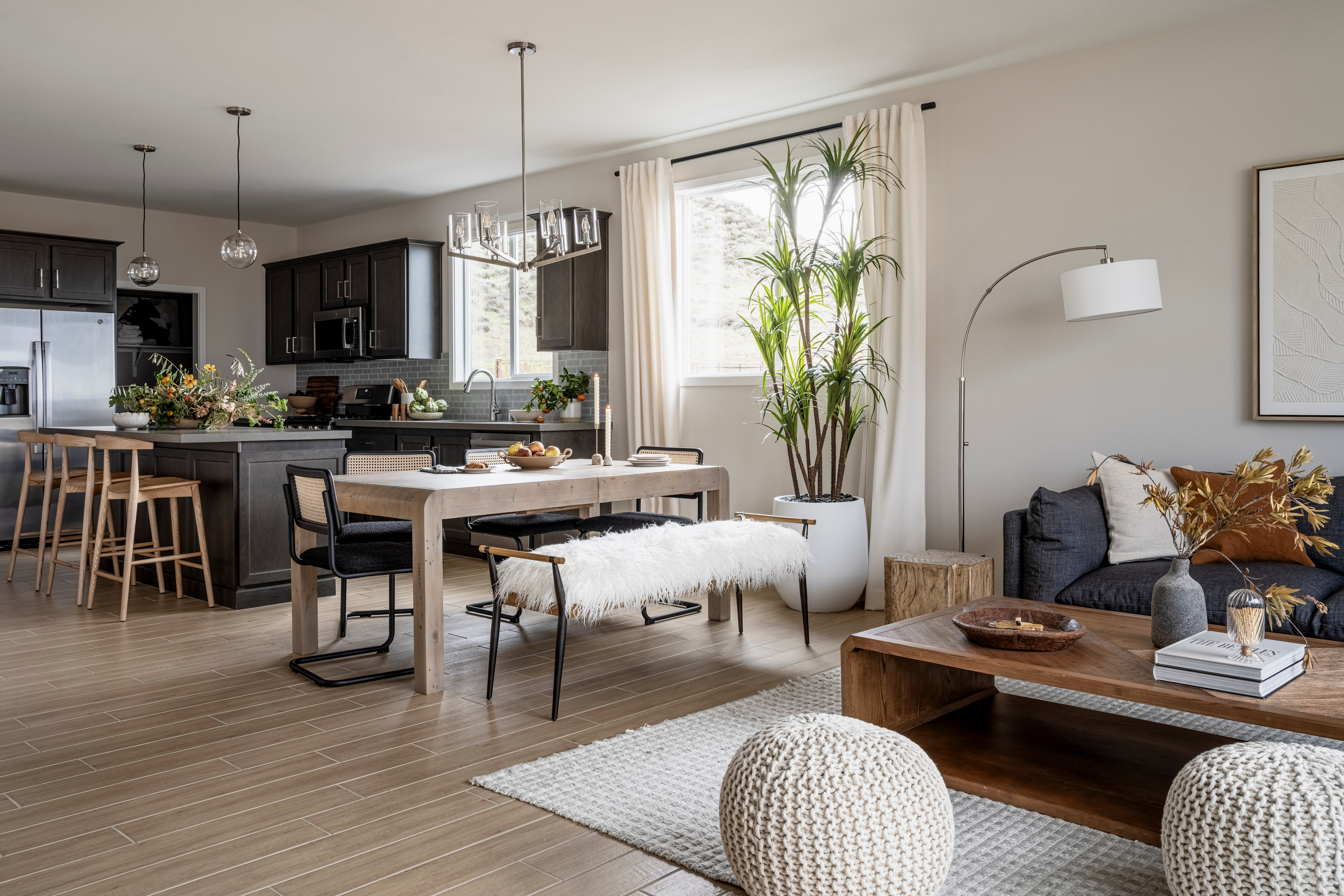 A modern and cozy open-concept living space with a kitchen, dining area, and living room, featuring a mix of dark and light tones, natural elements, and comfortable furnishings.