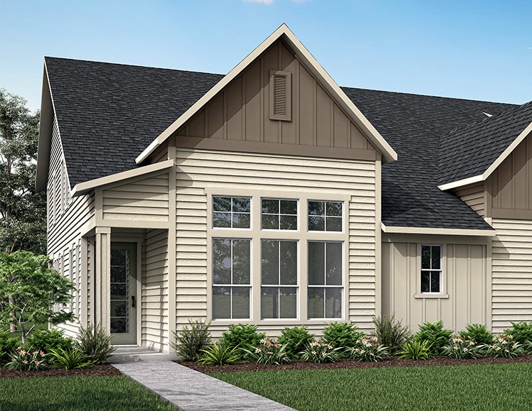 A two-story house with a gabled roof, wooden siding, and a covered porch sits on a grassy lawn surrounded by lush greenery.