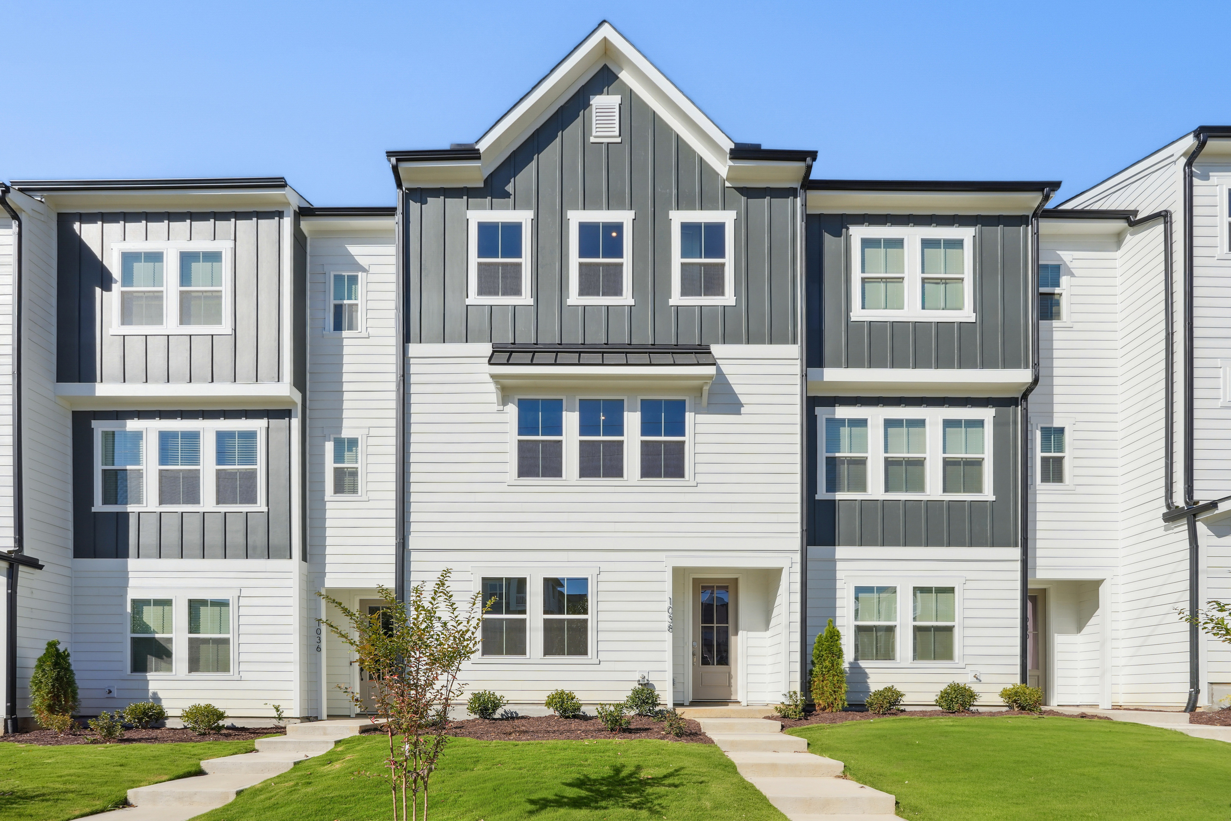 A multi-story residential building with a gray and white exterior, surrounded by a well-manicured lawn and landscaping.