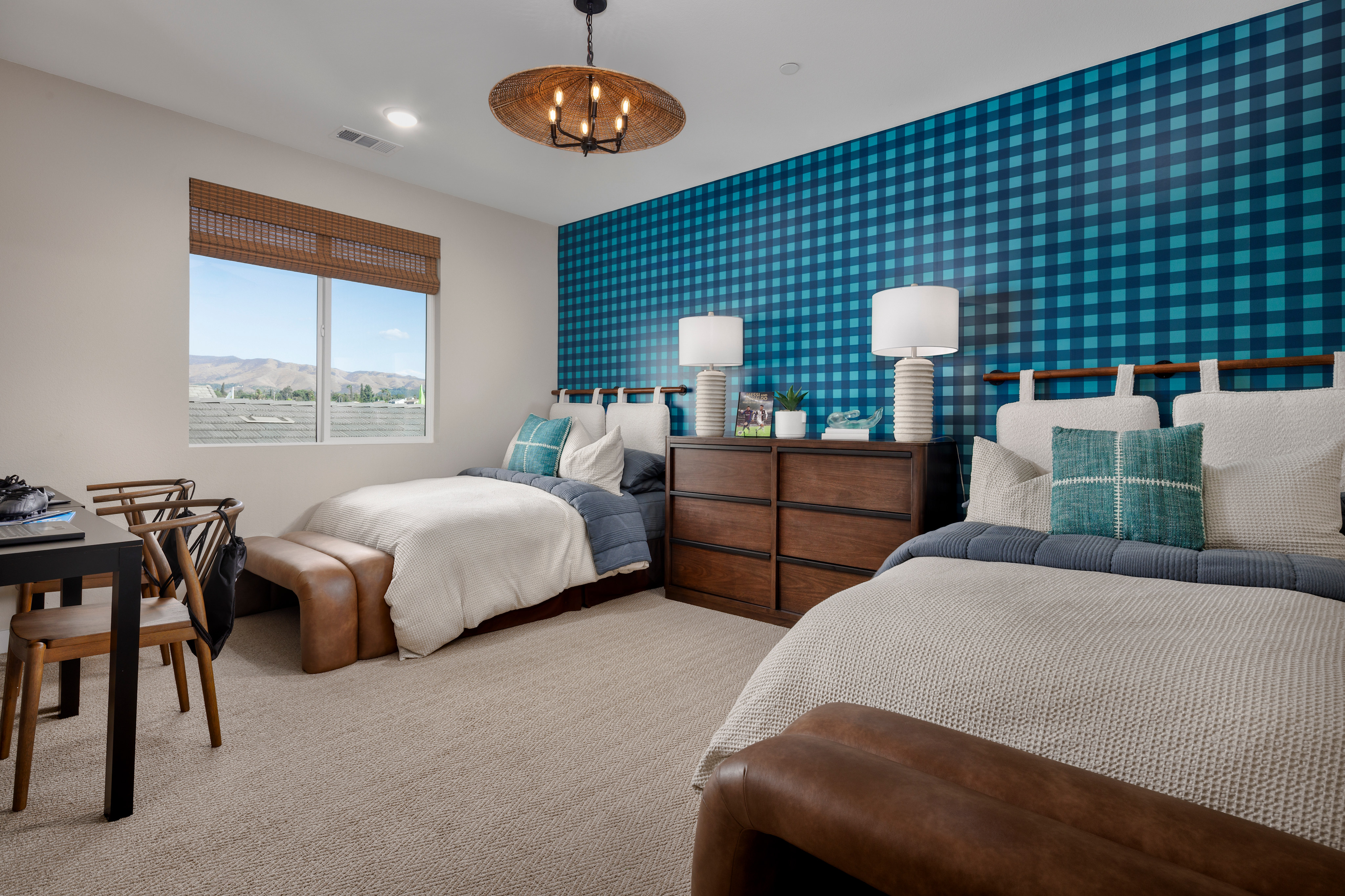 A cozy bedroom with a blue and white checkered accent wall, a wooden dresser, and two twin beds with neutral bedding.