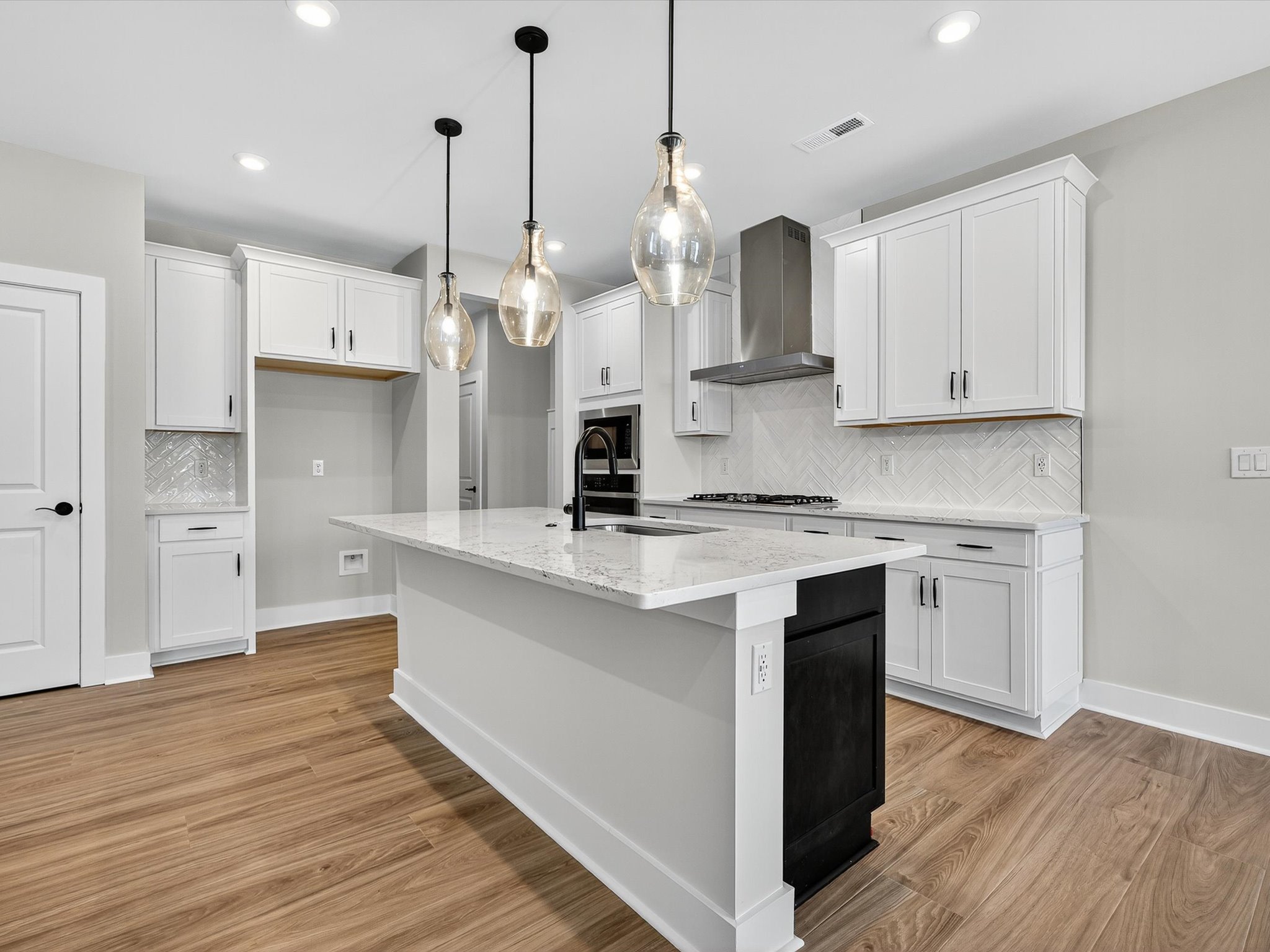 A modern, open-concept kitchen with white cabinets, a marble-topped island, and pendant lighting fixtures hanging above the island.