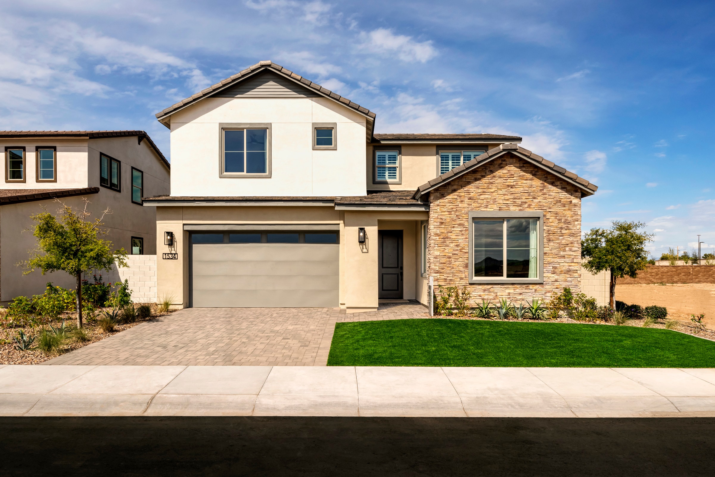 A two-story residential house with a garage, surrounded by a well-manicured lawn and set against a backdrop of a clear blue sky with scattered clouds.