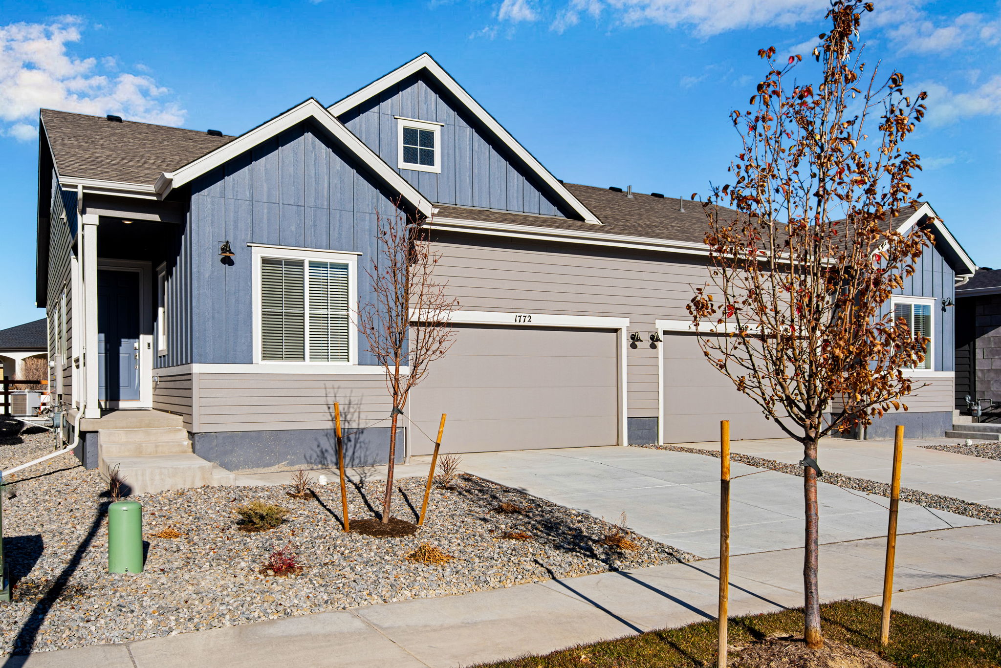 A modern two-story house with a gray exterior, a garage, and a landscaped front yard with small trees and gravel.