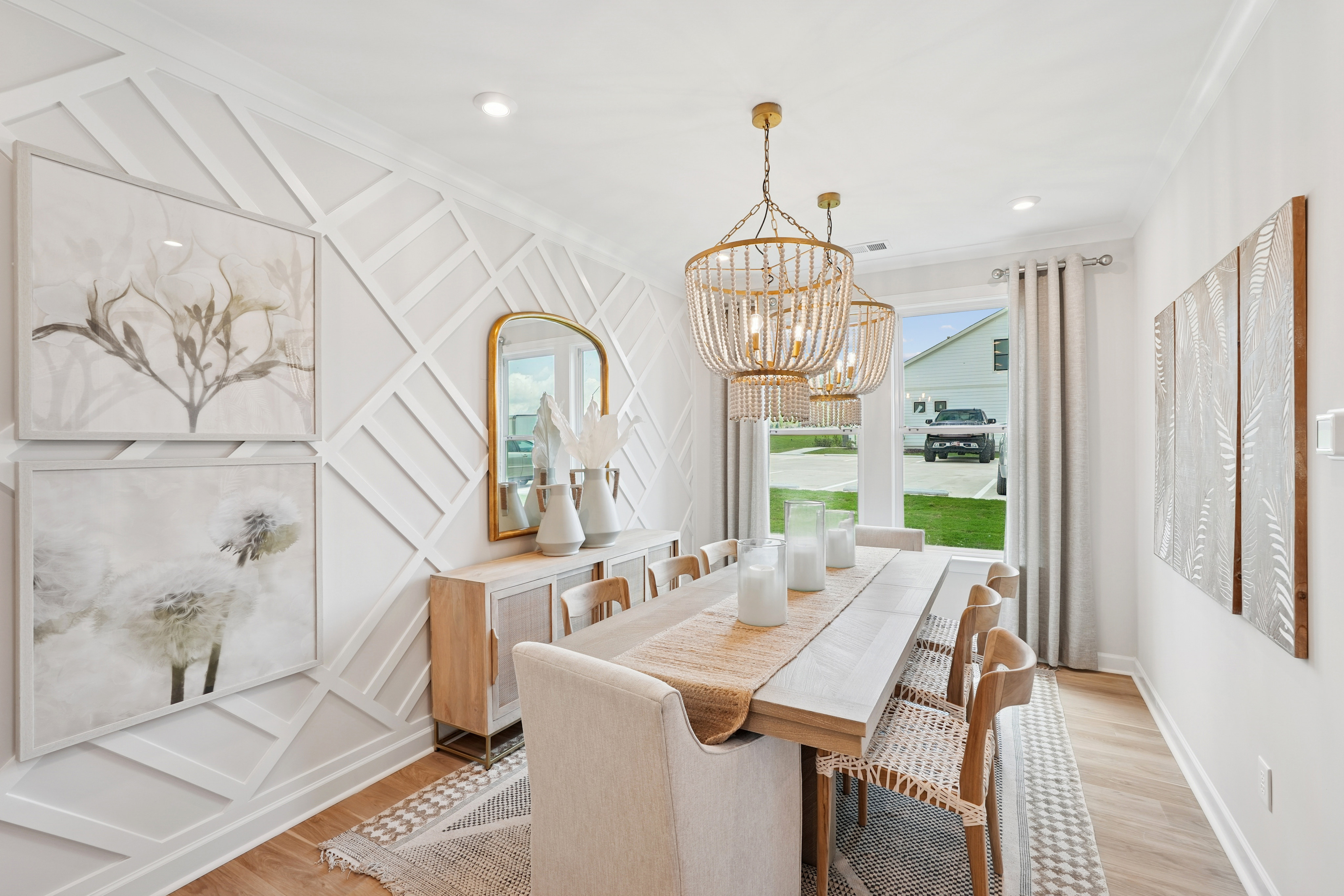 A modern and stylish dining room with a long wooden table, white chairs, and decorative wall panels, complemented by a chandelier and artwork on the walls.