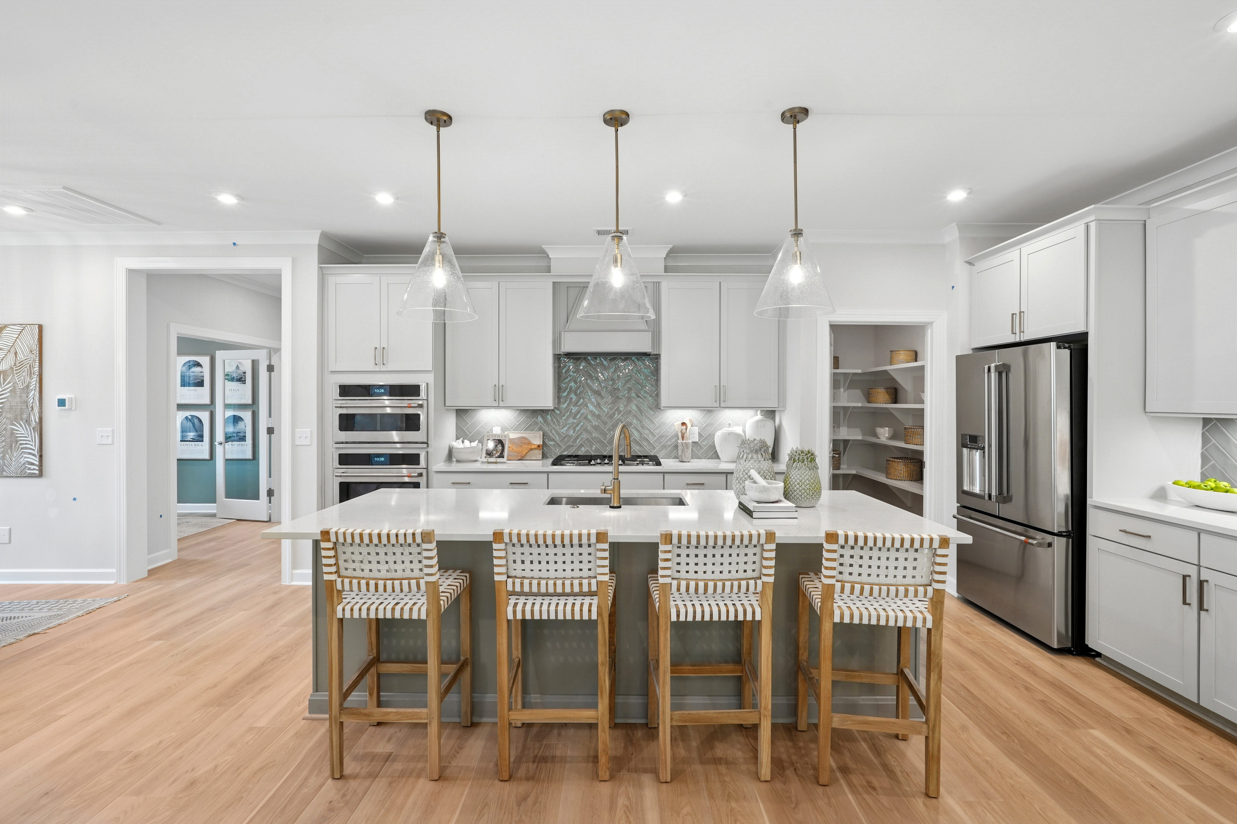 A modern, open-concept kitchen with white cabinets, stainless steel appliances, a large island with bar stools, and pendant lighting fixtures.