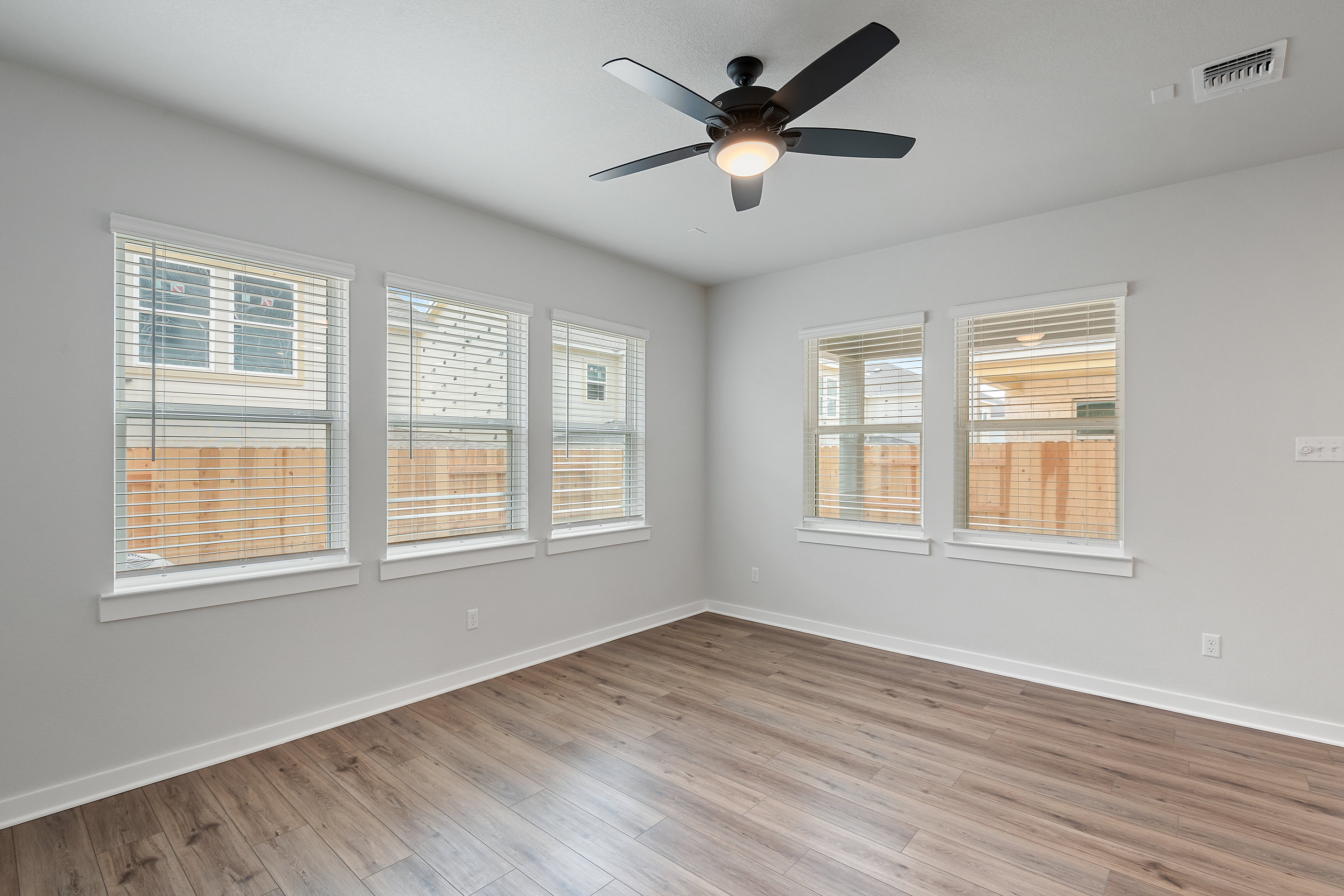 A bright and airy room with a ceiling fan, wooden floors, and large windows providing ample natural light.