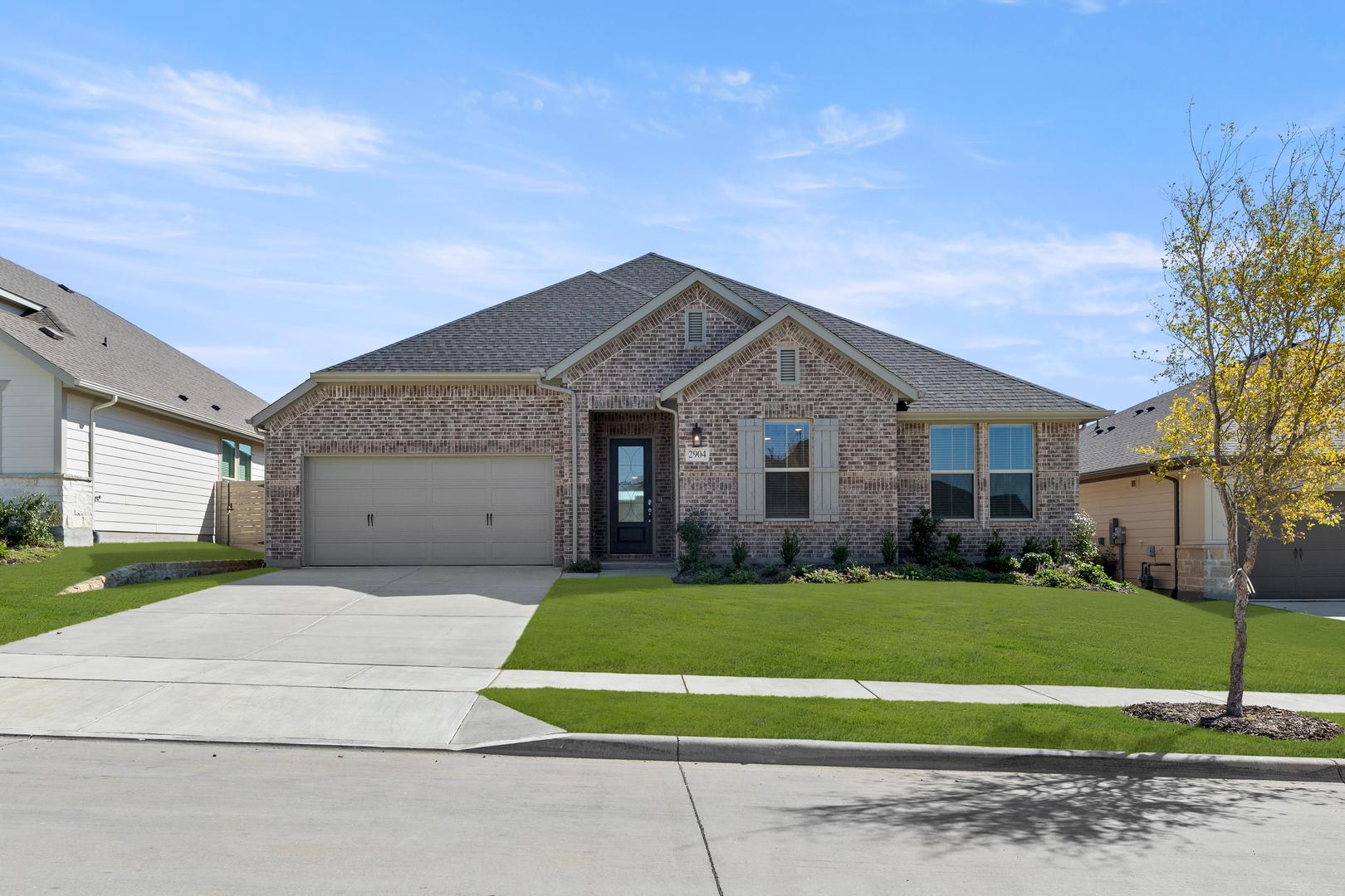 A single-story brick house with a gabled roof and a well-manicured lawn in the foreground, set against a clear blue sky with scattered clouds.