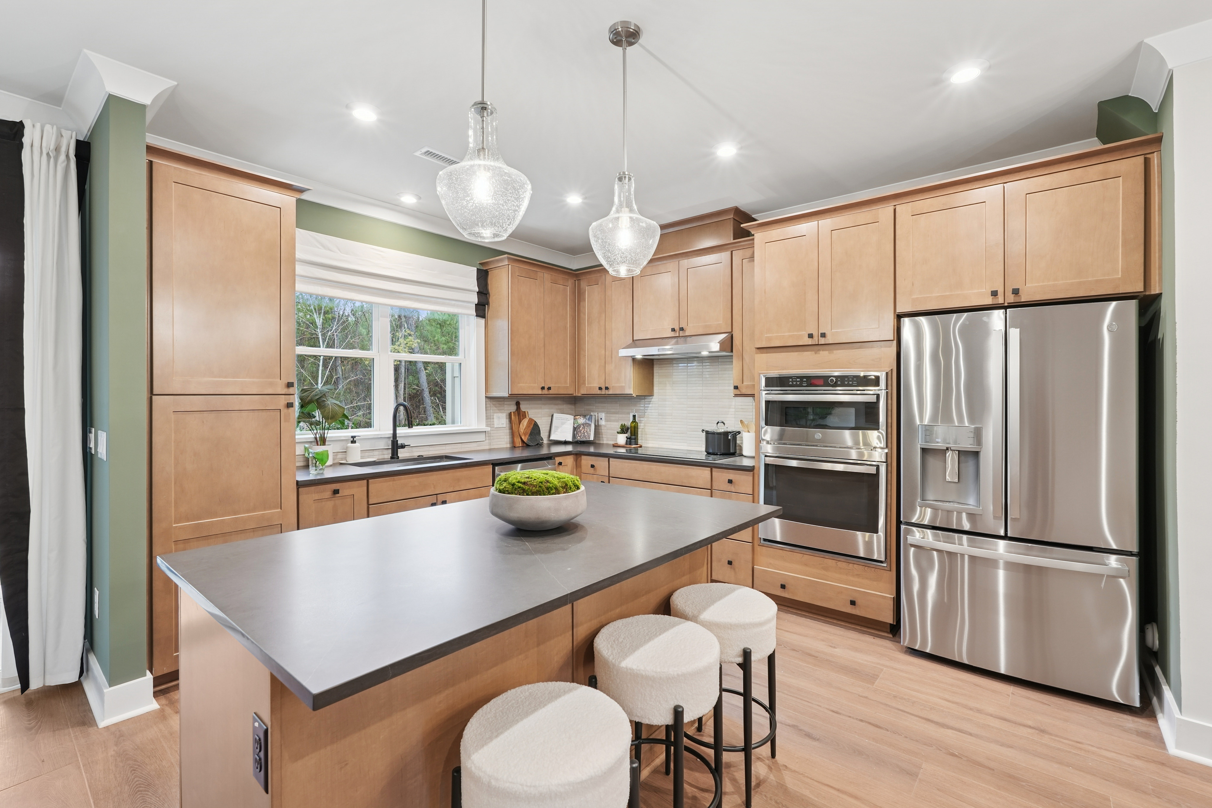 A modern, well-equipped kitchen with light wood cabinets, stainless steel appliances, and a central island with stools for seating.