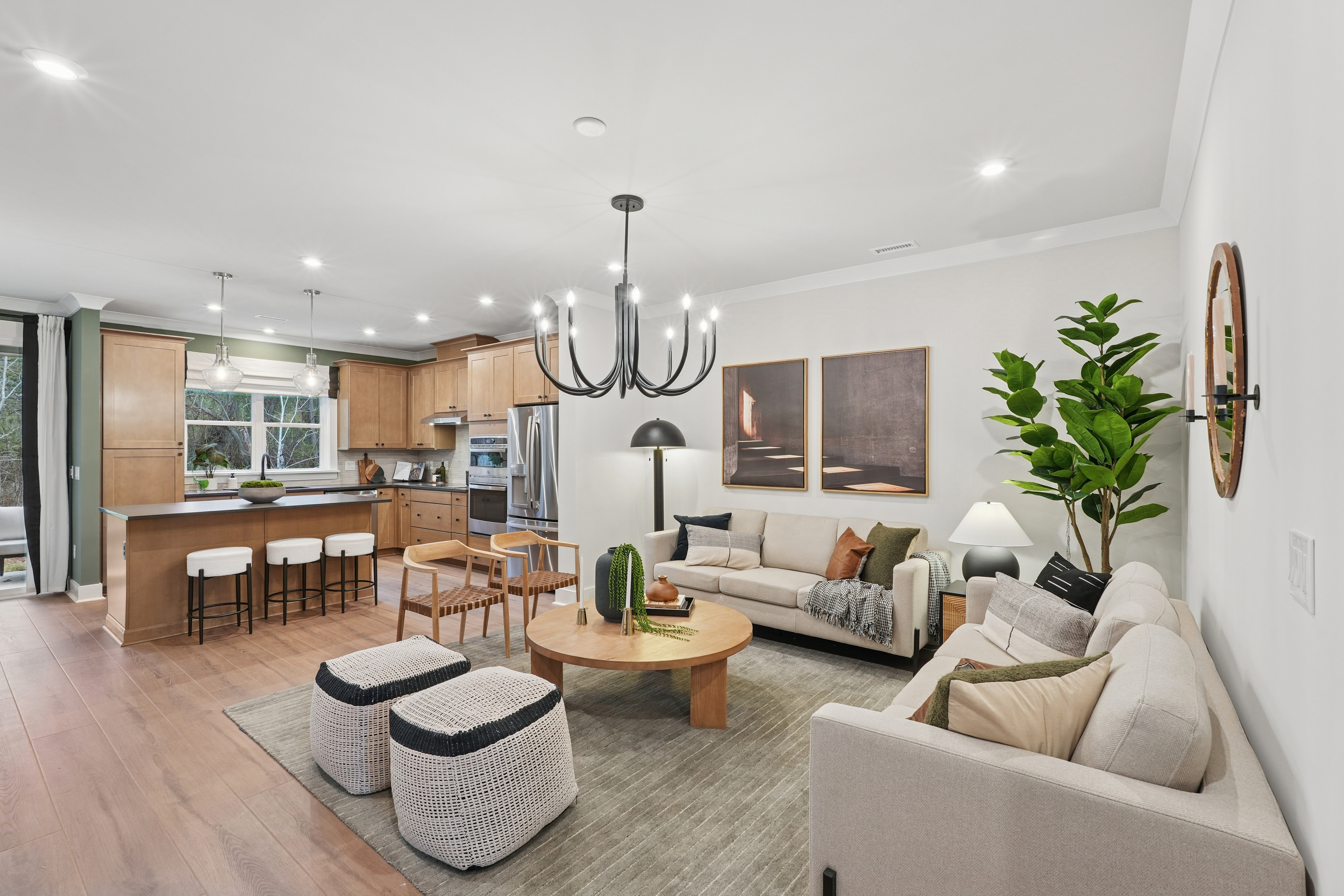A modern and cozy open-concept living room and kitchen area with wooden floors, neutral-toned furniture, and various decorative elements such as plants and artwork.