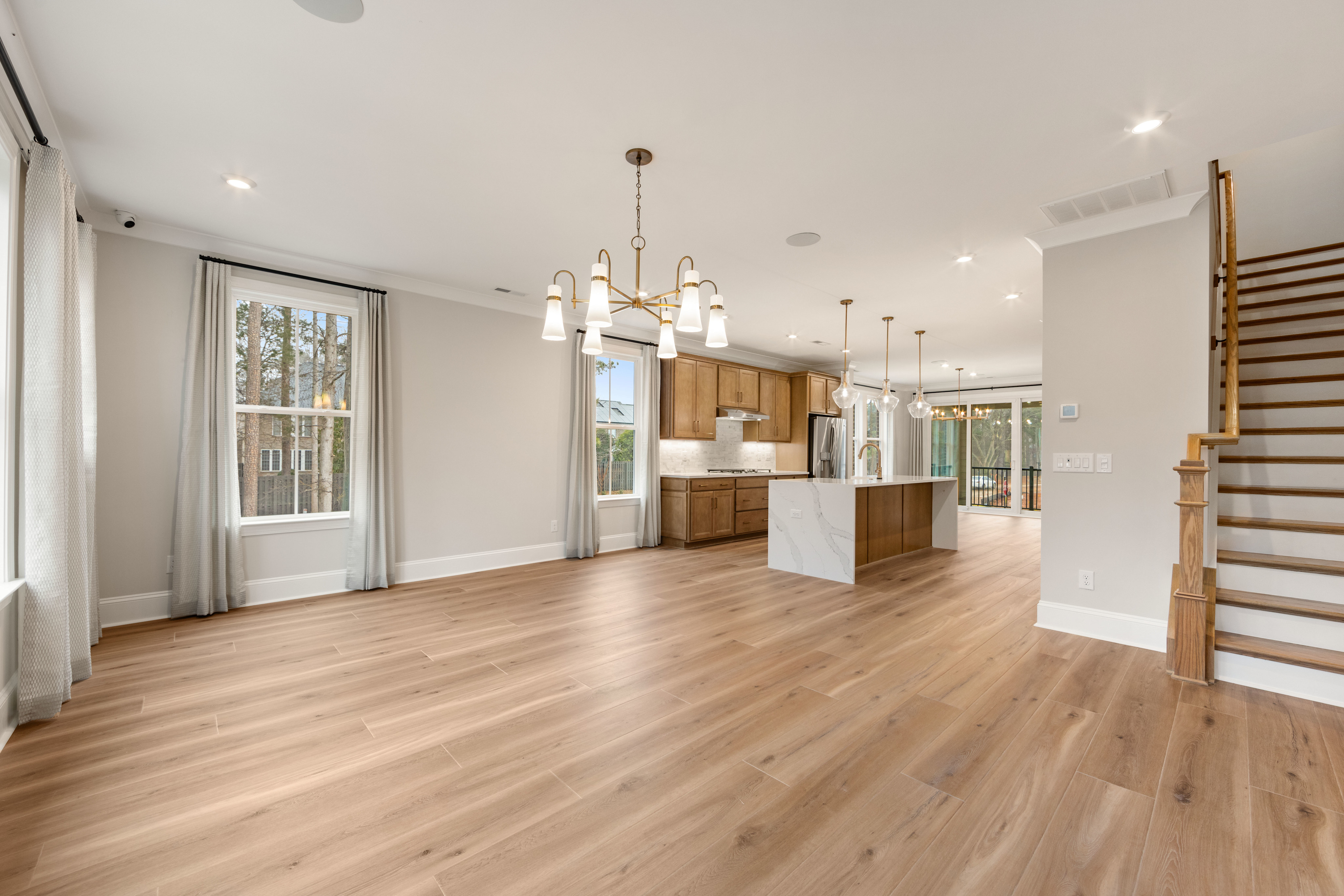 A spacious and modern open-plan living area with hardwood floors, a kitchen with wooden cabinets, and a staircase leading to an upper level.
