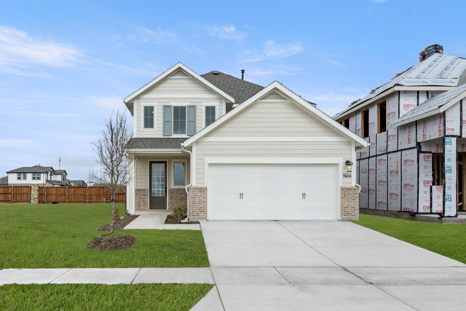 A two-story house with a white exterior, a garage, and a well-manicured lawn in the foreground, set against a clear blue sky with some clouds in the background.