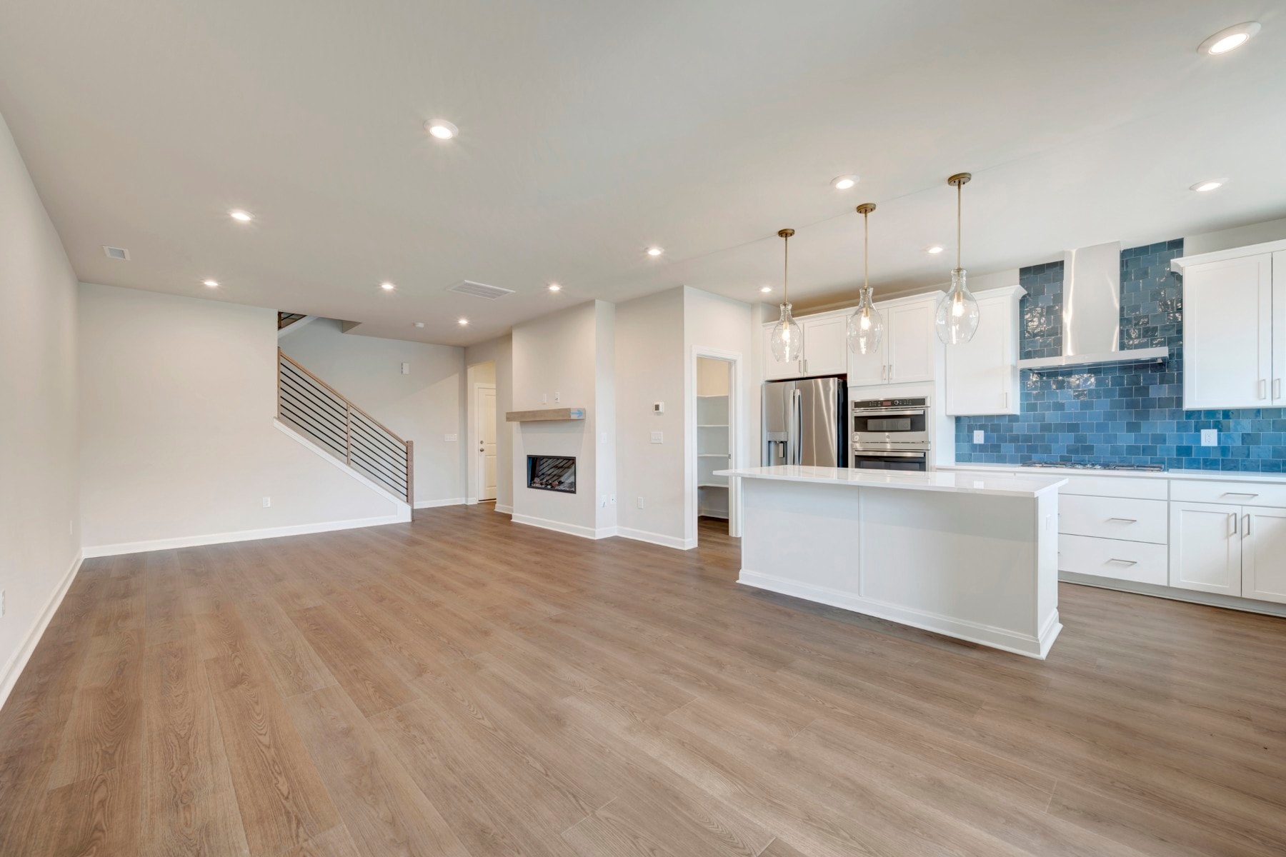A modern, open-concept kitchen and living room with white cabinets, hardwood floors, and pendant lighting.