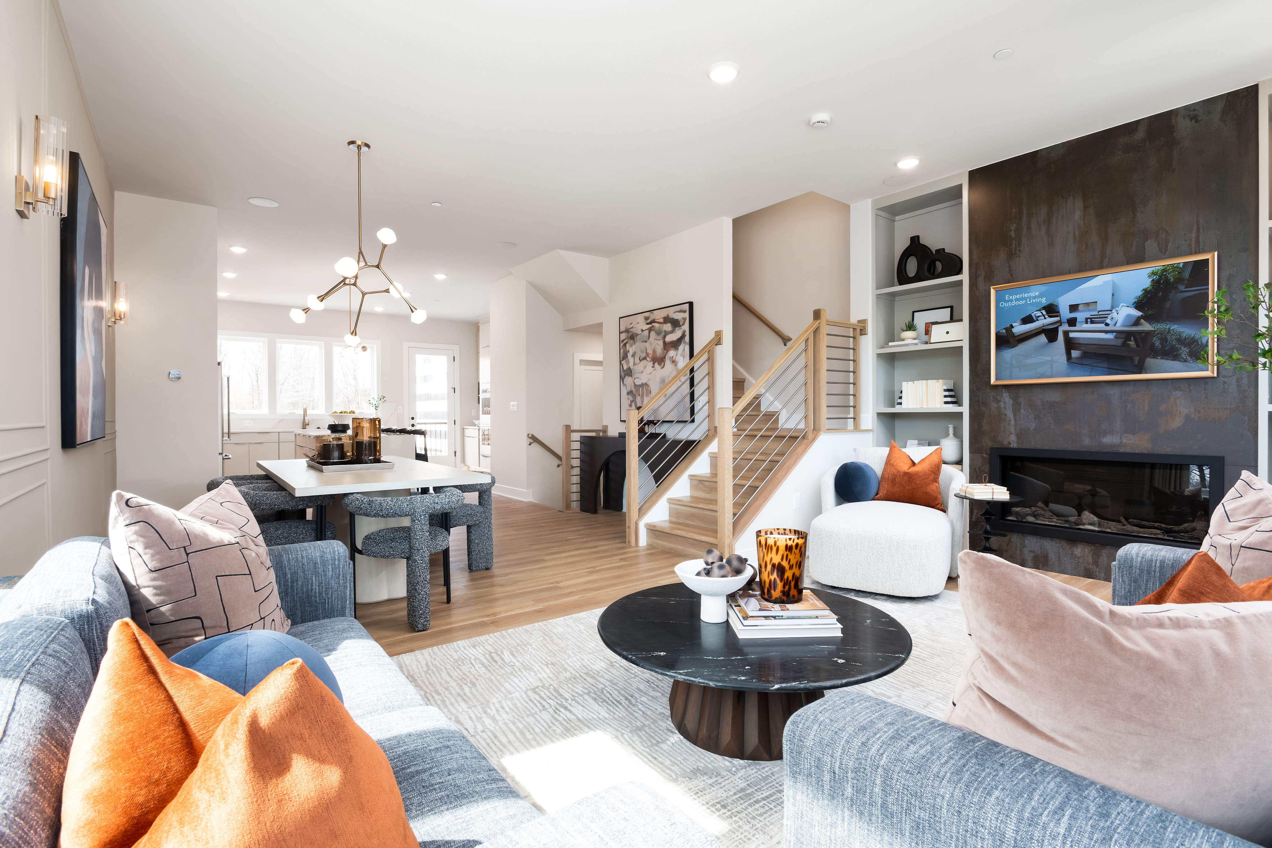 A modern and stylish living room with a cozy seating area, a fireplace, and a staircase leading to the upper level, complemented by a dining area and an open kitchen in the background.