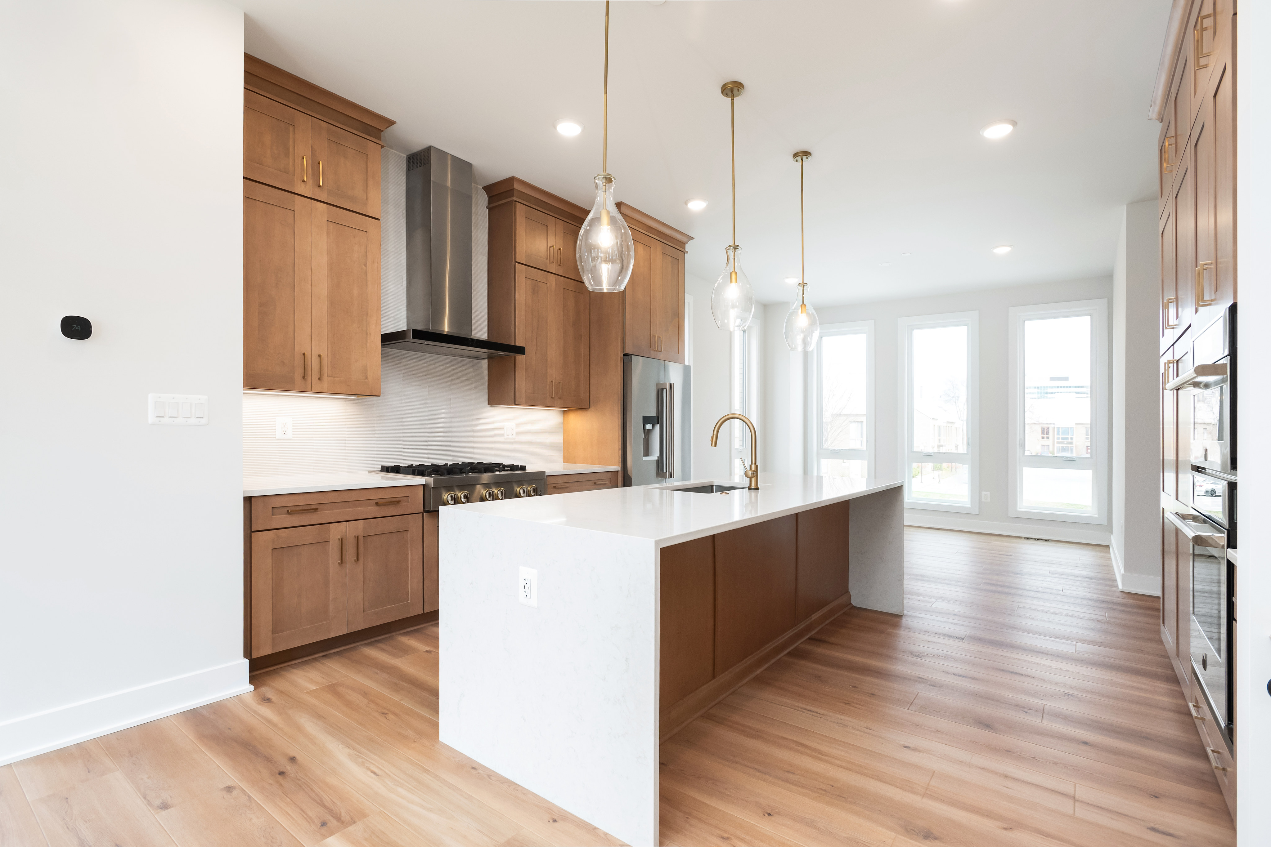 A modern, open-concept kitchen with wooden cabinets, white countertops, and pendant lighting fixtures, leading into a bright and airy living space with hardwood floors.