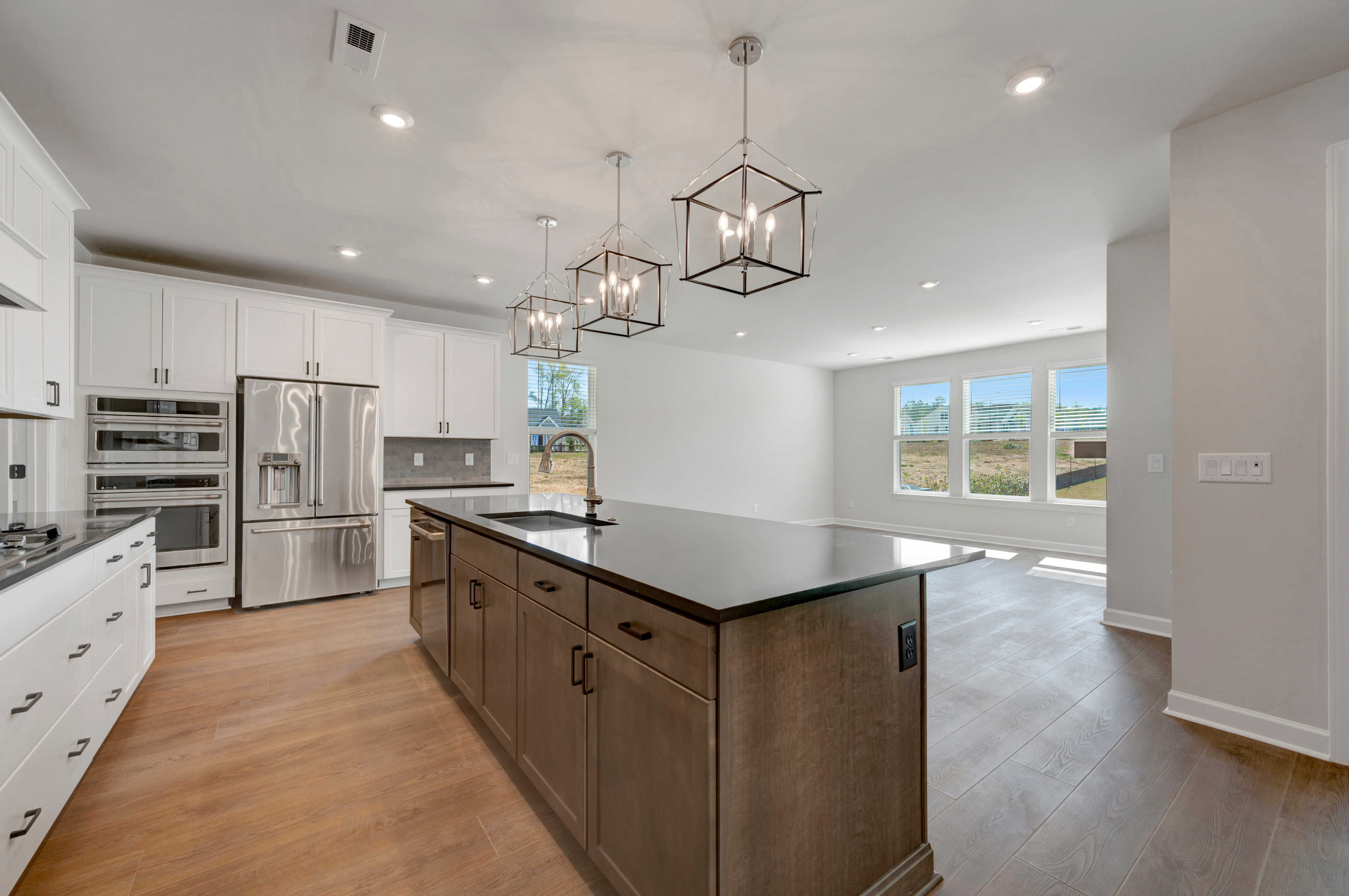 A modern, open-concept kitchen with white cabinets, dark wood island, and stylish pendant lighting fixtures.