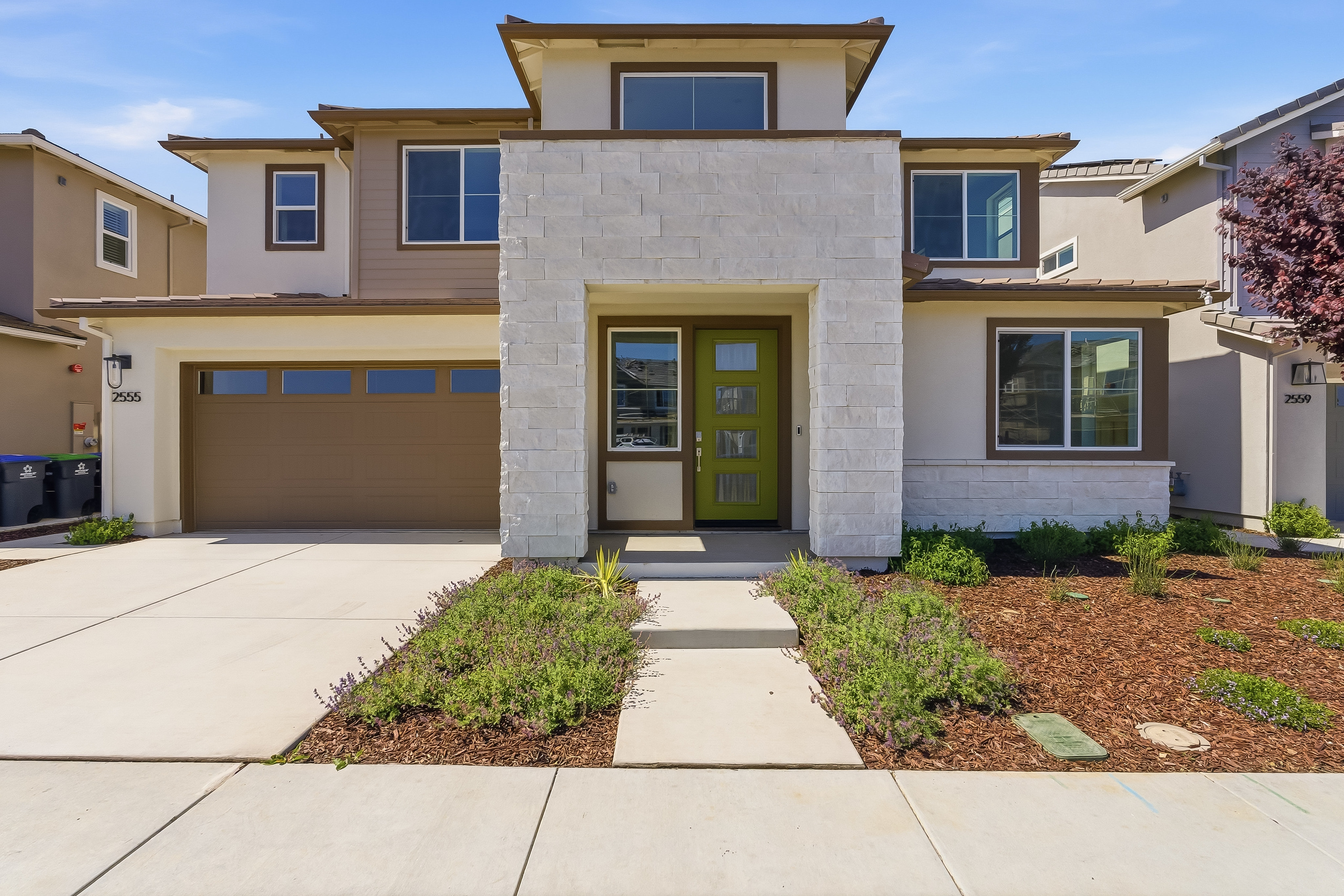 A modern two-story house with a green front door, surrounded by a landscaped yard and a paved driveway leading to a garage.