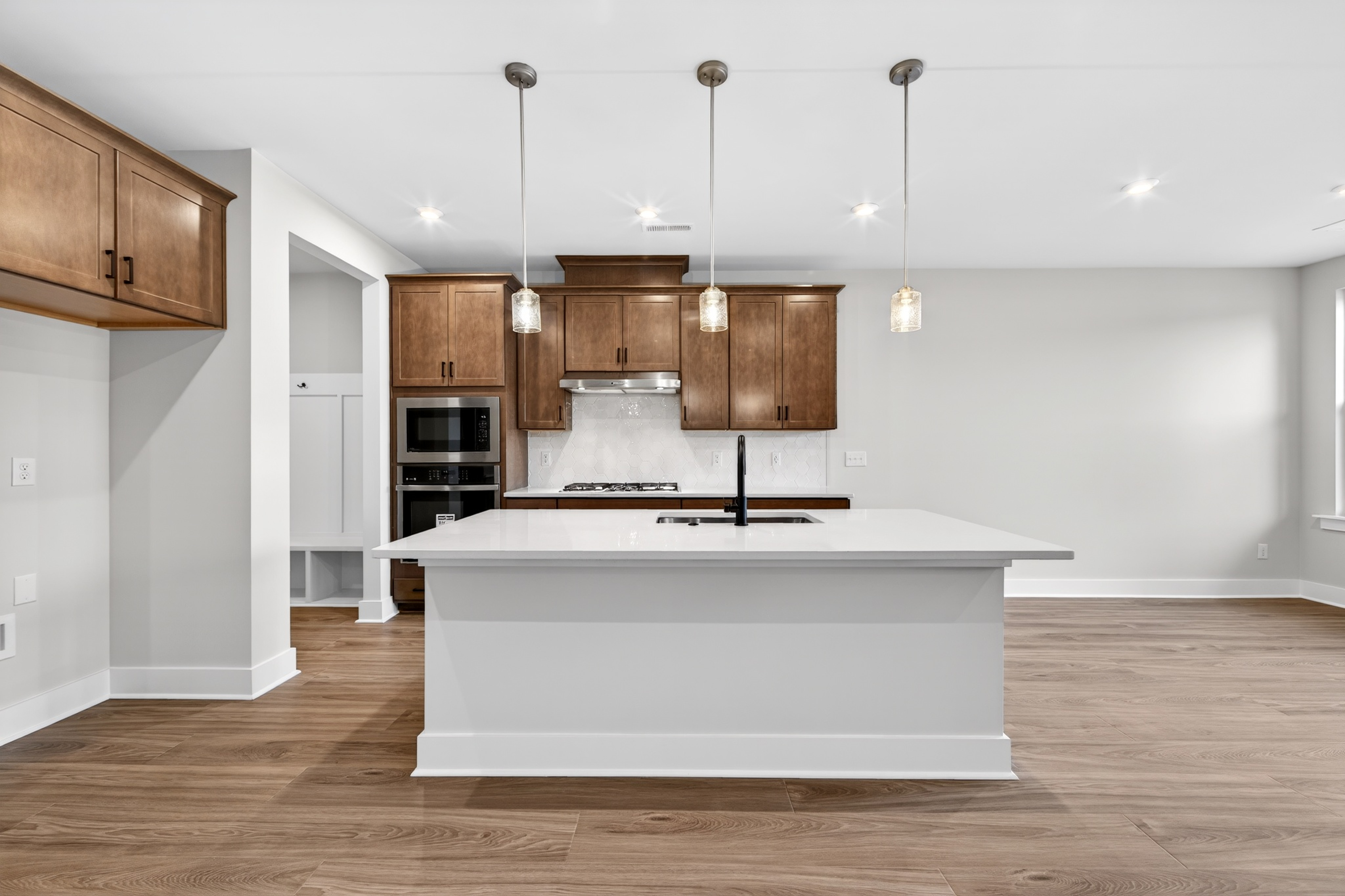 A modern kitchen features a white island in the foreground and dark wood cabinets with stainless steel appliances in the background.