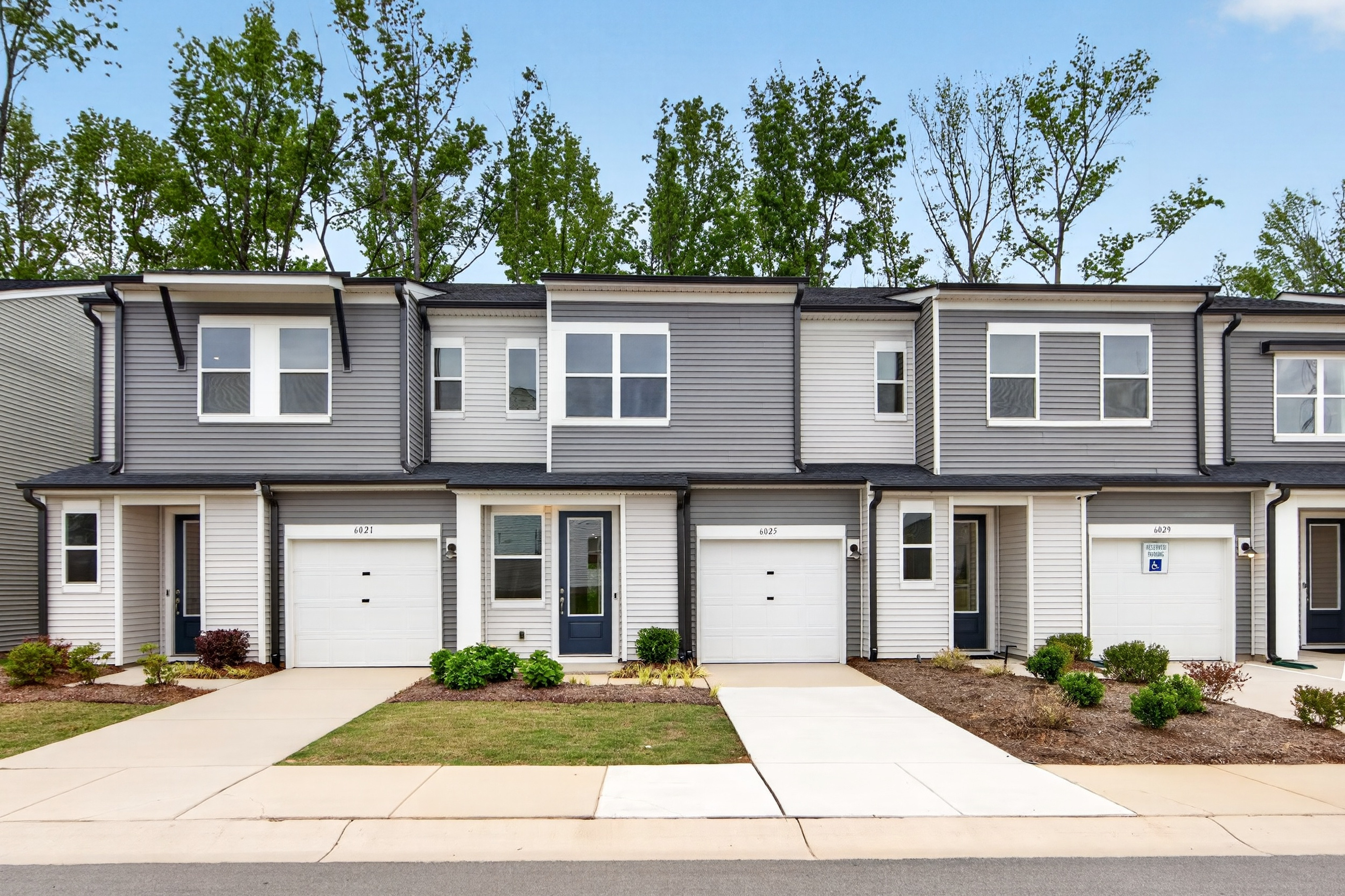 Modern townhouses with manicured lawns in the foreground are set against a backdrop of lush green trees.