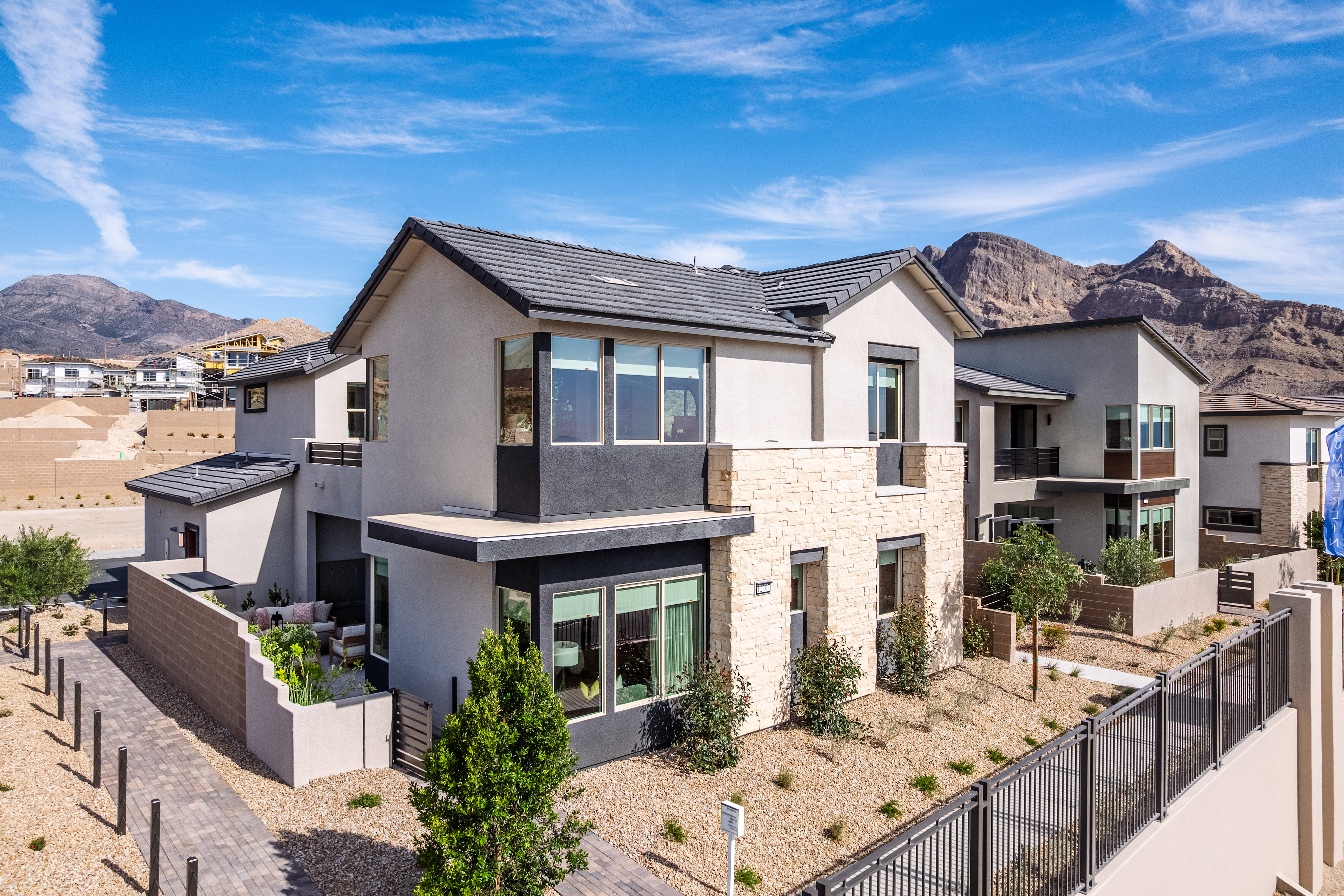 Modern homes with stone and stucco exteriors are nestled against a backdrop of arid, mountainous terrain under a clear blue sky.