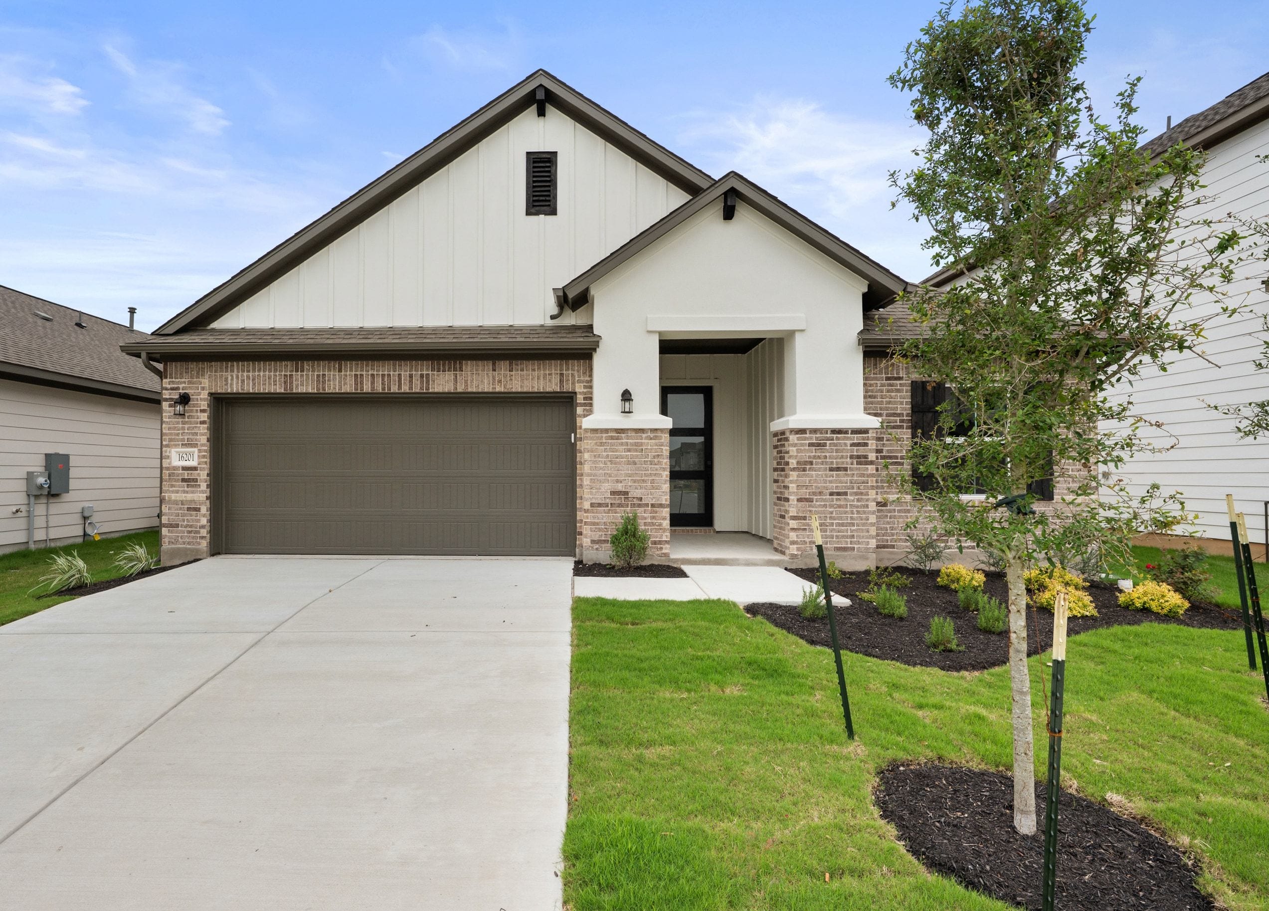 A modern house with a brick and white exterior and a concrete driveway sits in front of a clear blue sky with scattered clouds.