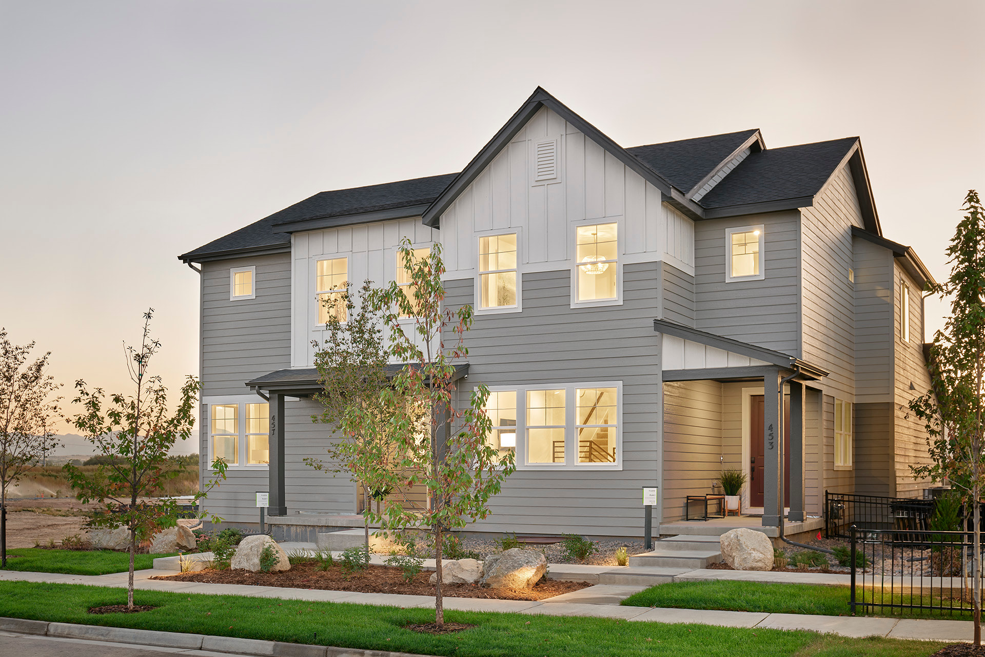 A modern gray and white townhouse with illuminated windows stands in the foreground, while a soft, hazy sky forms the background.
