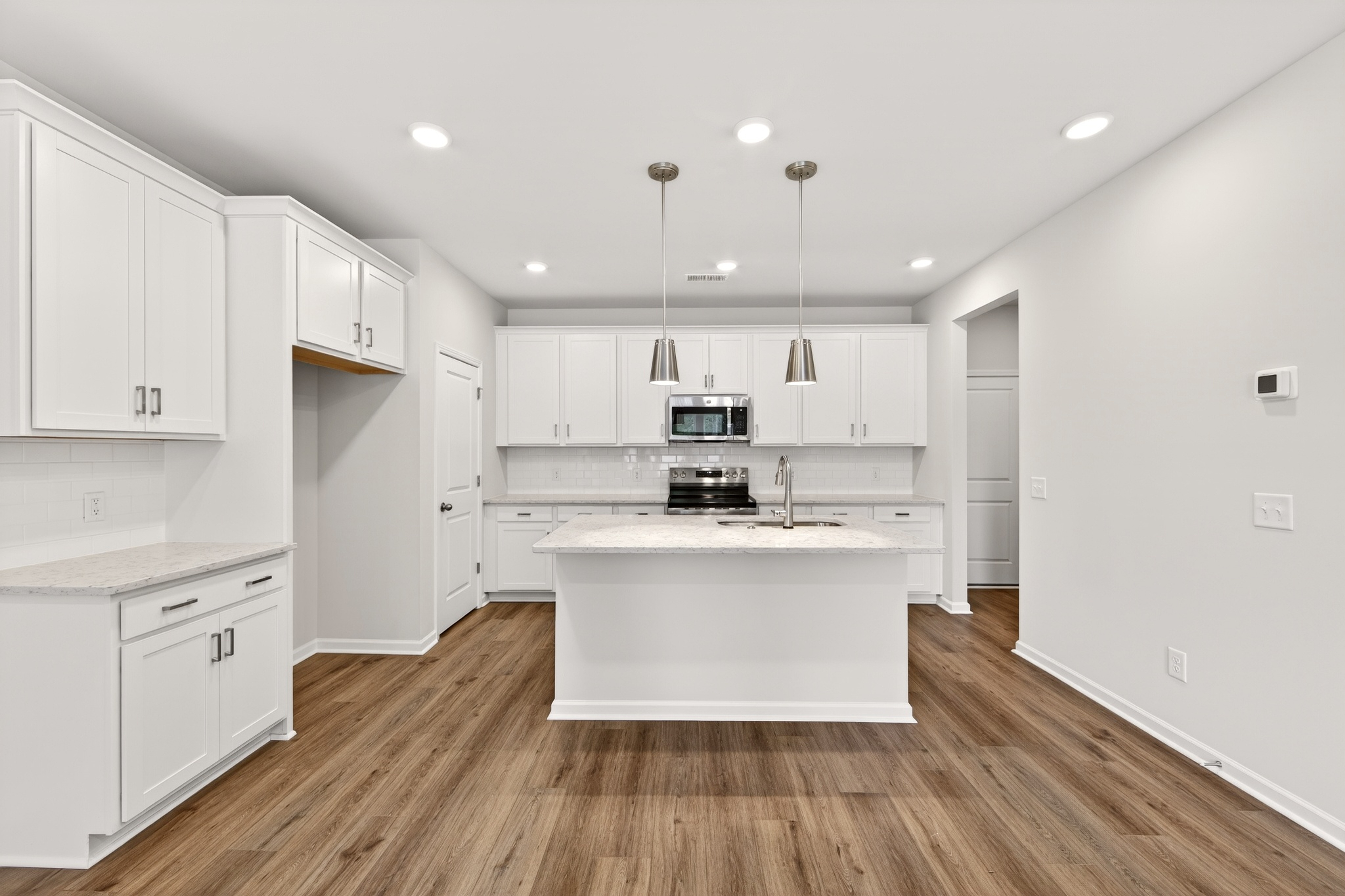 A modern white kitchen with a central island and stainless steel appliances is visible, with a light wood-plank floor in the foreground and white walls in the background.
