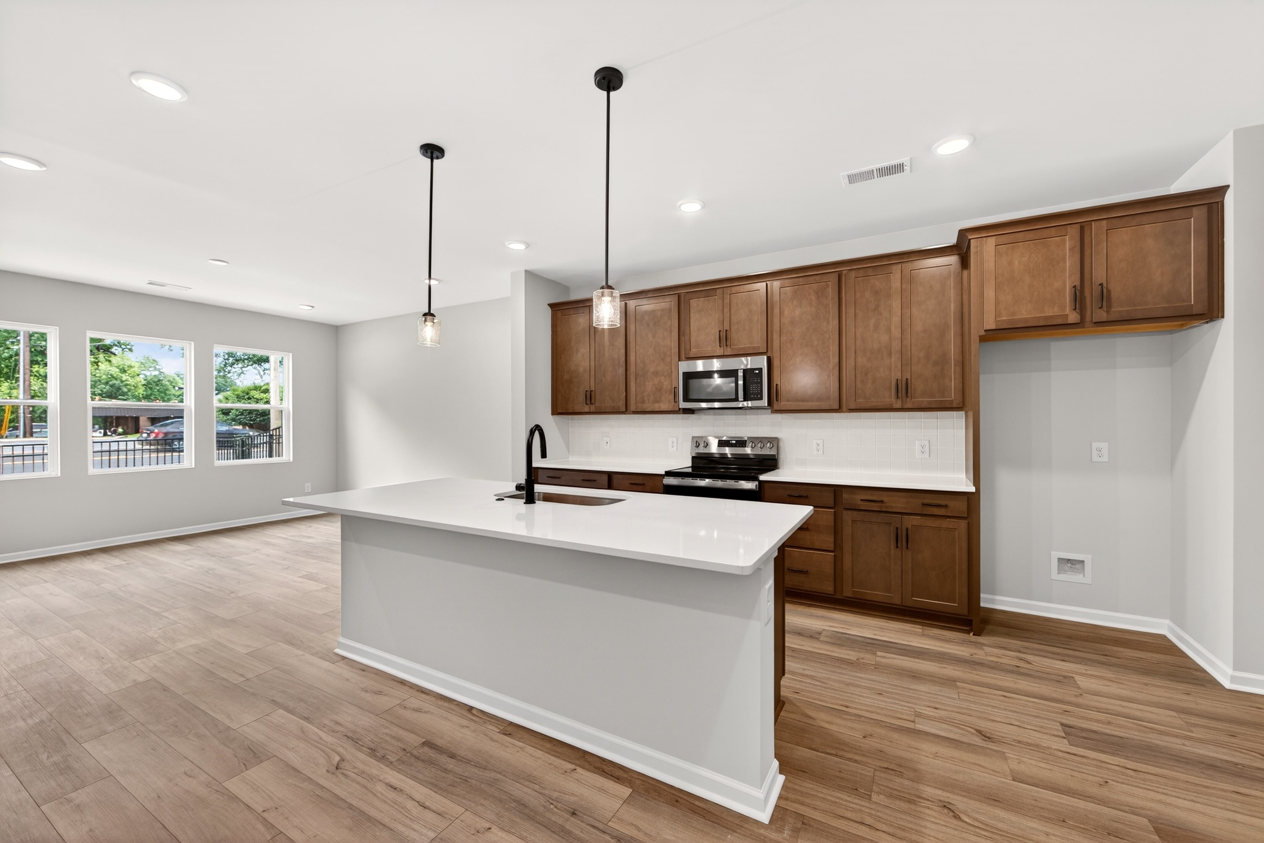 A modern kitchen island with a white countertop and dark faucet is in the foreground, while dark wood cabinets and stainless steel appliances fill the background.