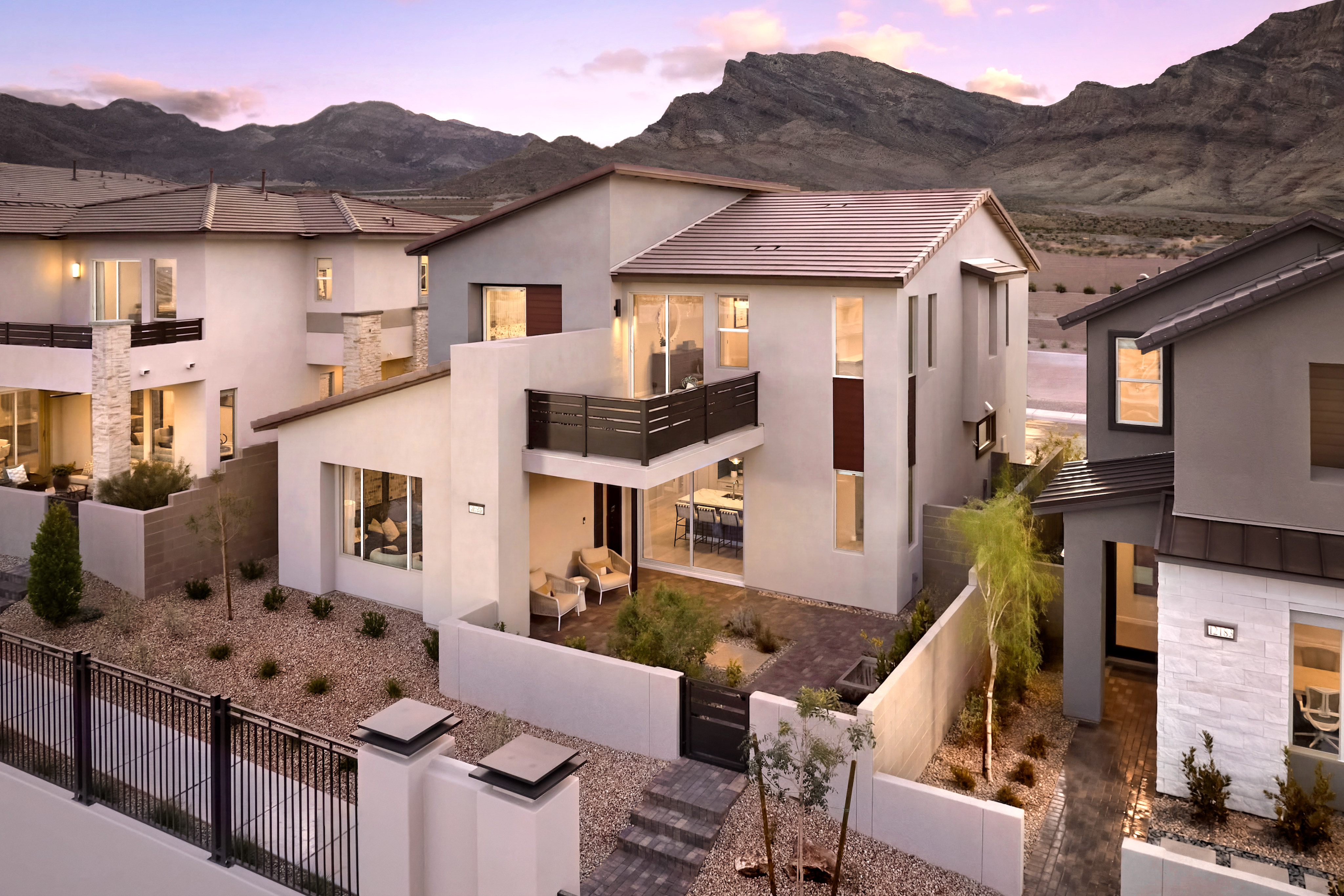 Modern homes with desert landscaping in the foreground are set against a backdrop of rugged mountains under a twilight sky.