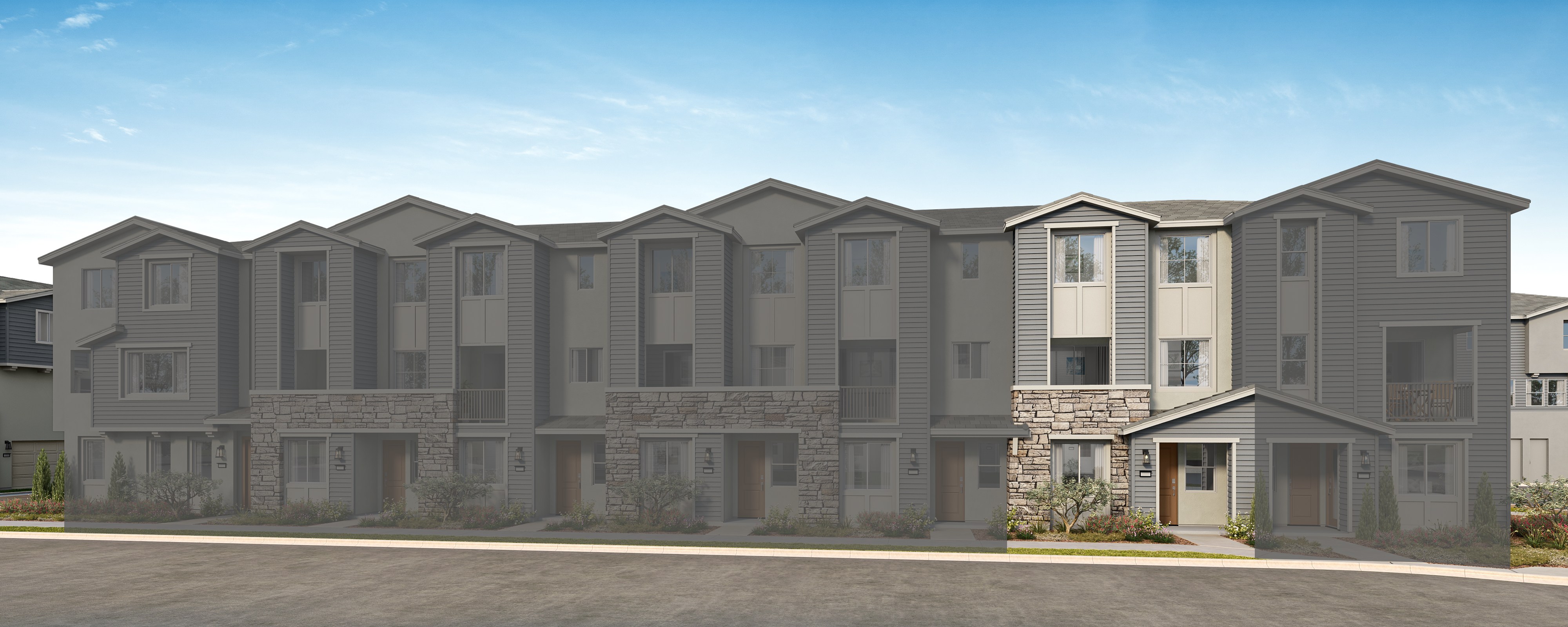 A row of modern, multi-story townhouses with gray siding and stone accents, set against a clear blue sky with fluffy white clouds.