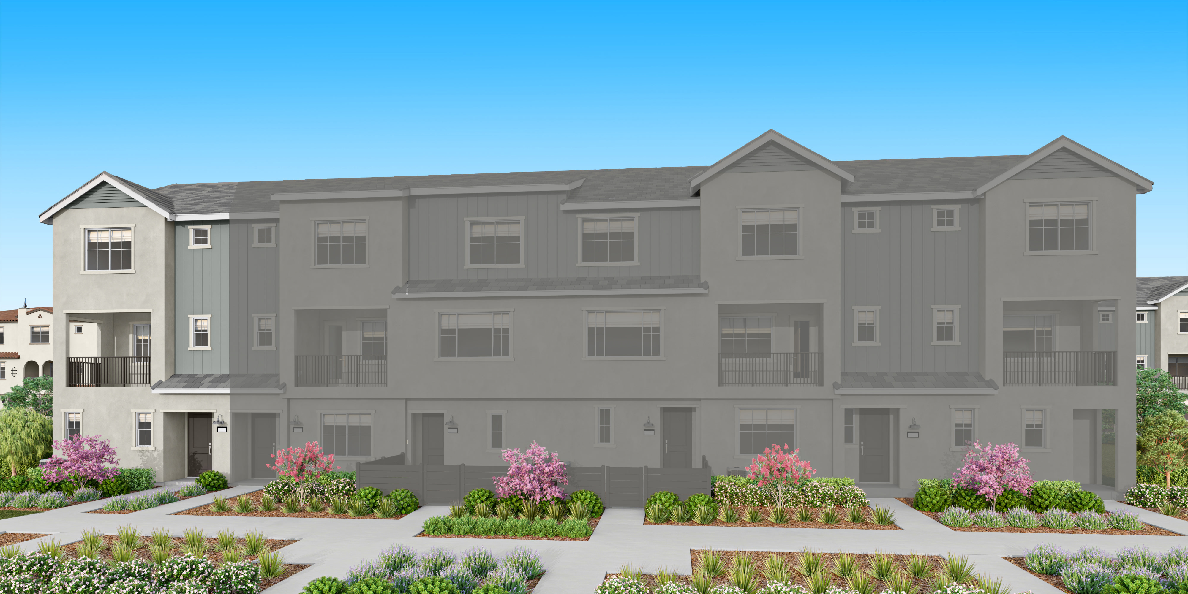 A row of modern townhouses with manicured landscaping and flowering trees in the foreground stands against a clear blue sky.