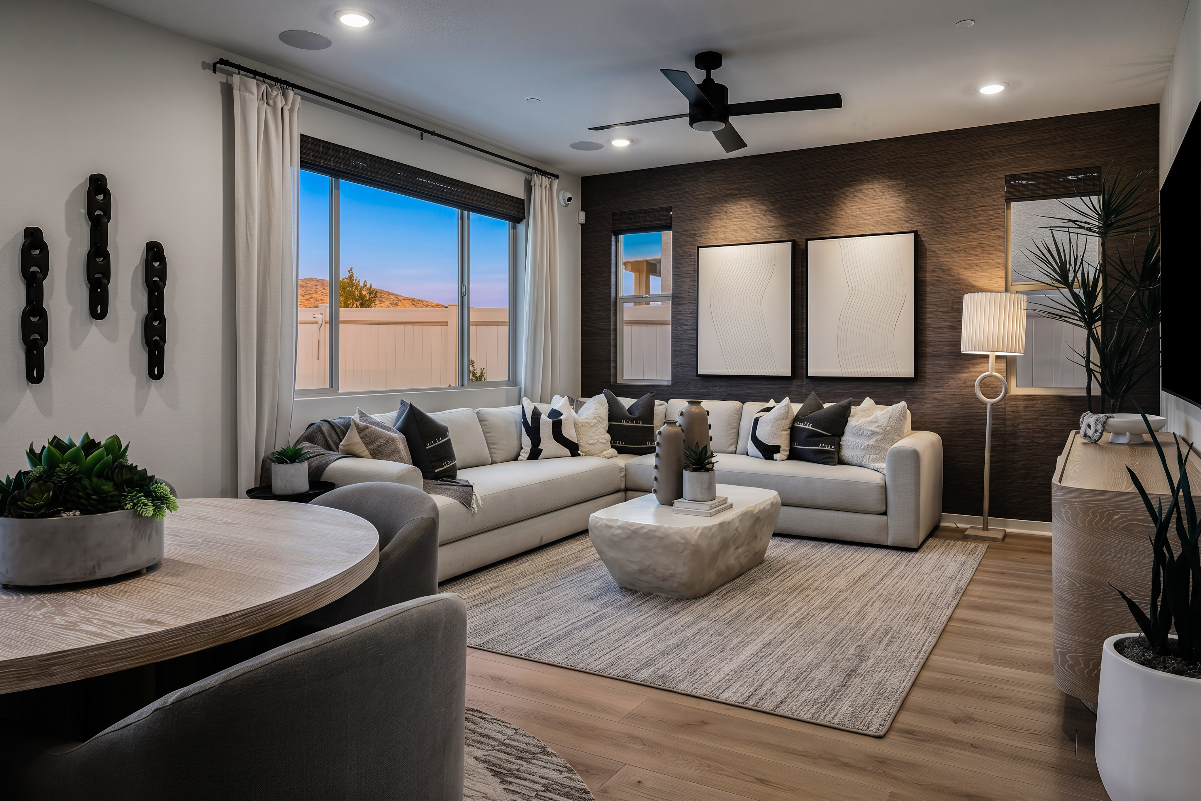 A modern living room with a sectional sofa and coffee table in the foreground, and a large window with a view of a suburban landscape in the background.