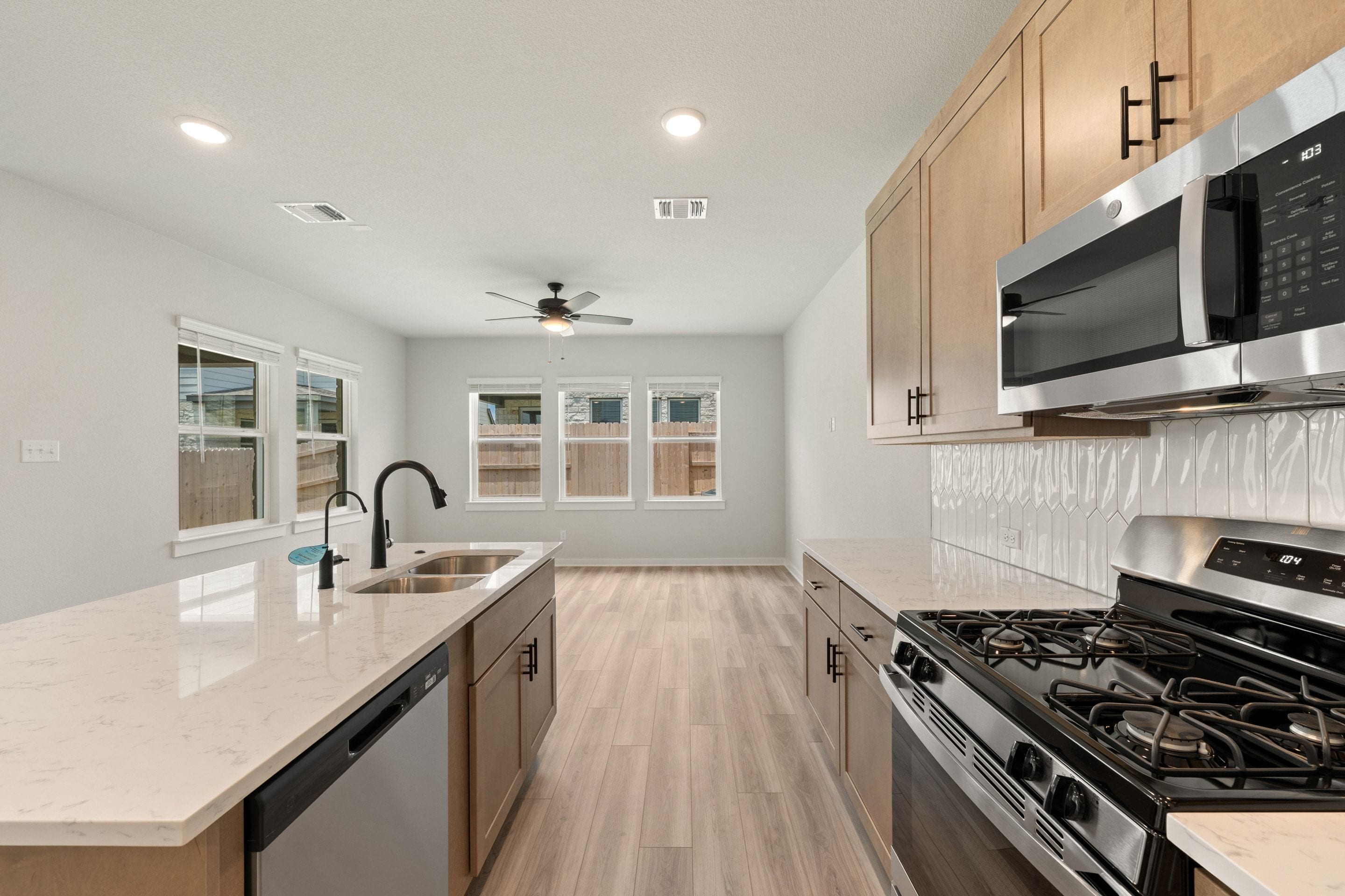 A modern kitchen with a white quartz island in the foreground and a dining area with large windows in the background.