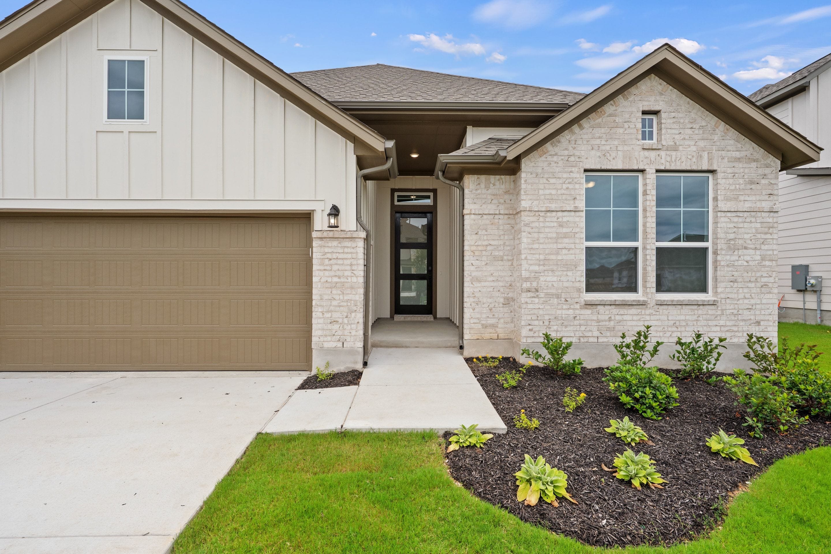 A modern house with a white brick facade and a beige garage door sits in front of a clear blue sky.