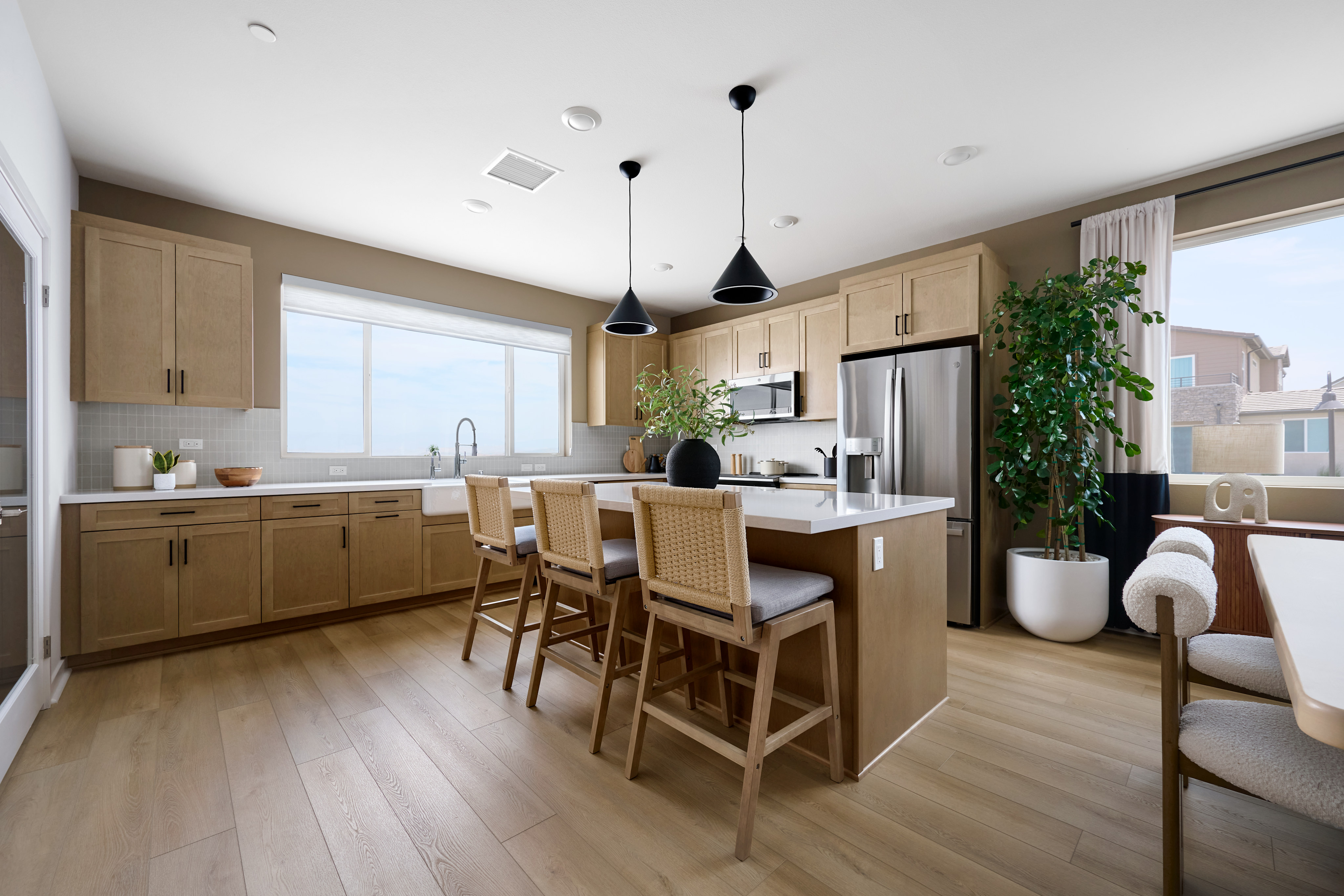 A modern kitchen with a large island and bar stools in the foreground, and a window overlooking houses in the background.