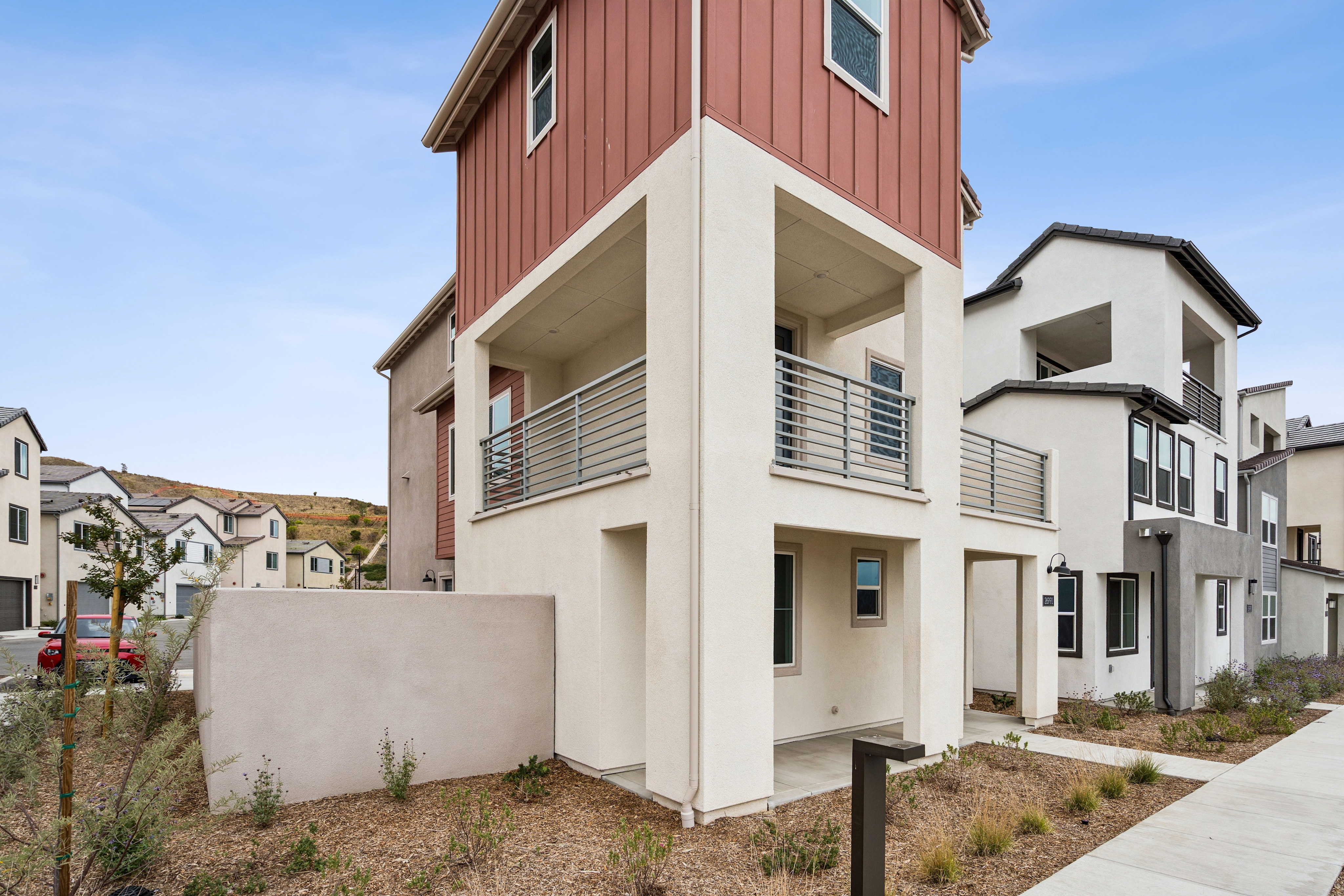 A modern townhouse with a red upper story stands in the foreground, while a row of similar houses stretches into the background under a cloudy sky.